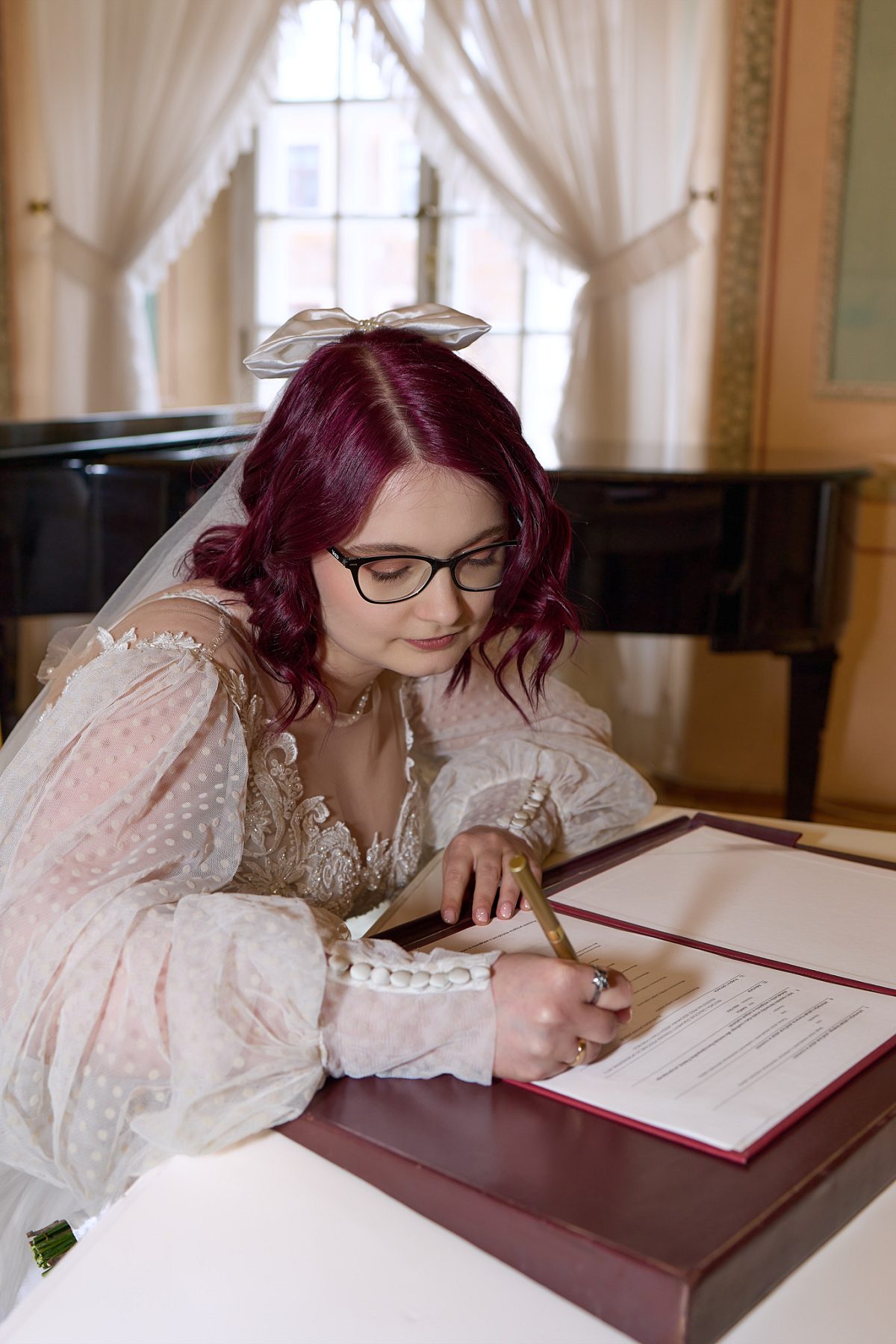 Bride with burgundy hair in a lace dress signing the marriage documents