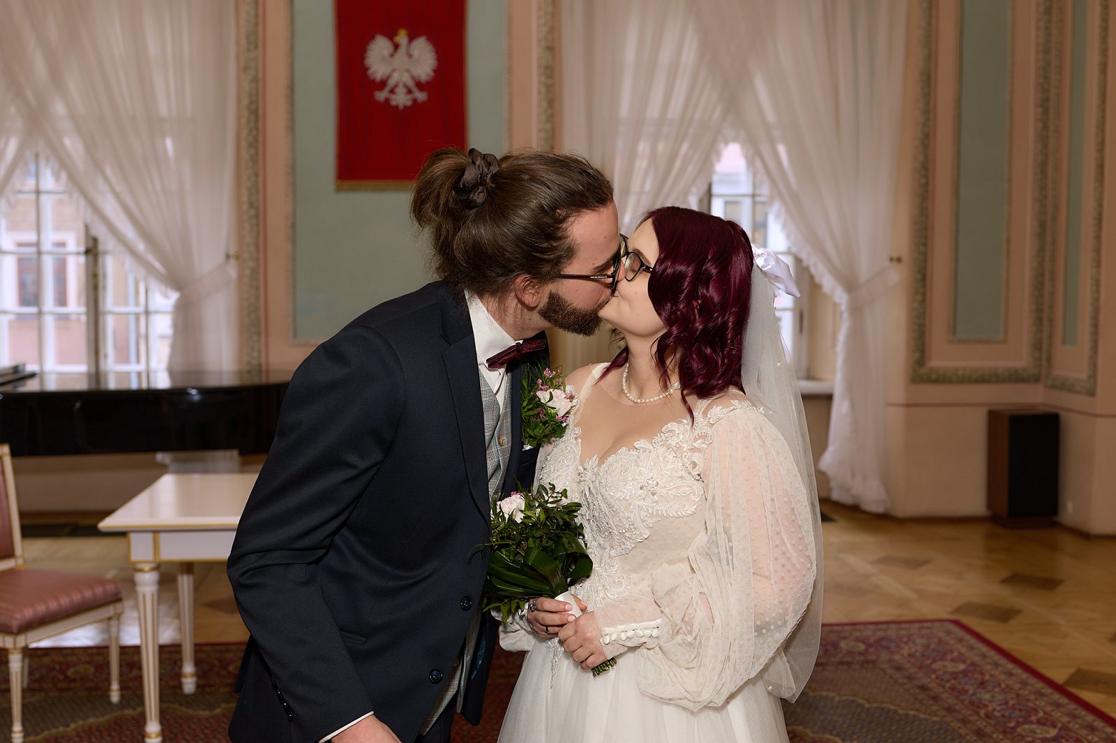 Newlyweds kissing in the civil wedding ceremony room beneath the Polish coat of arms