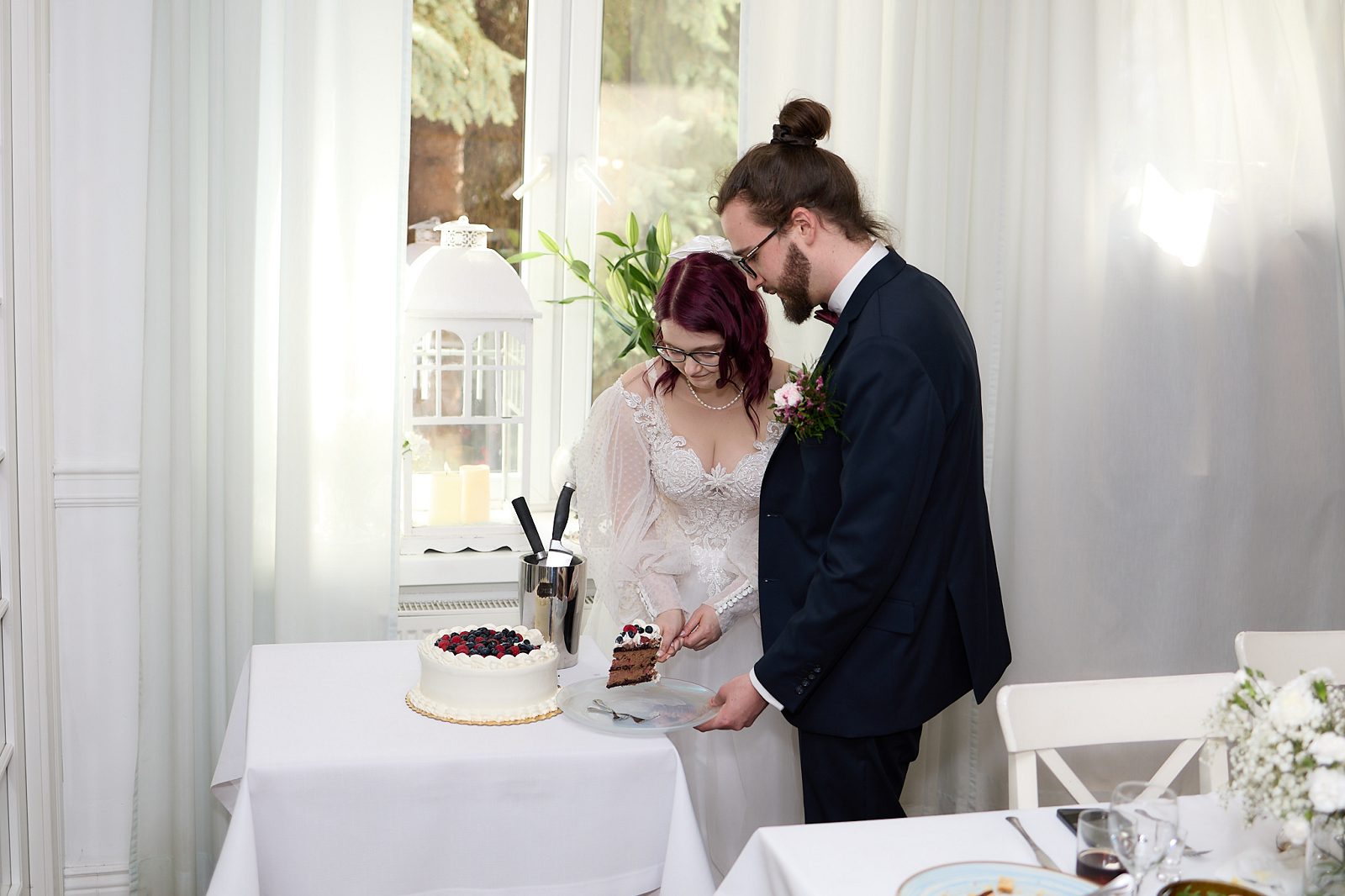 Bride placing a slice of wedding cake on a plate held by the groom