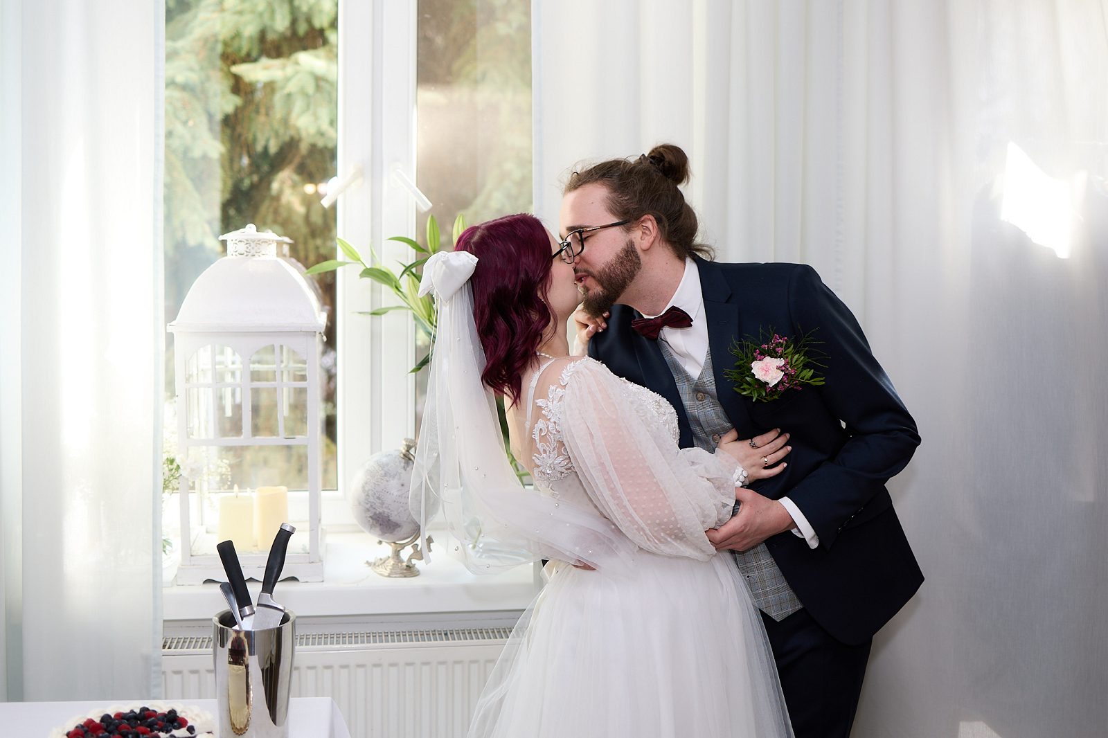 Newlyweds kissing by a window beside their wedding cake
