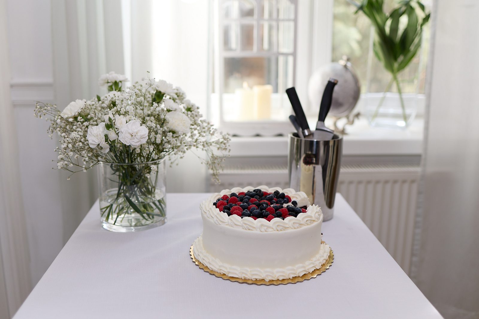 White wedding cake topped with raspberries and blueberries beside a bouquet of white flowers