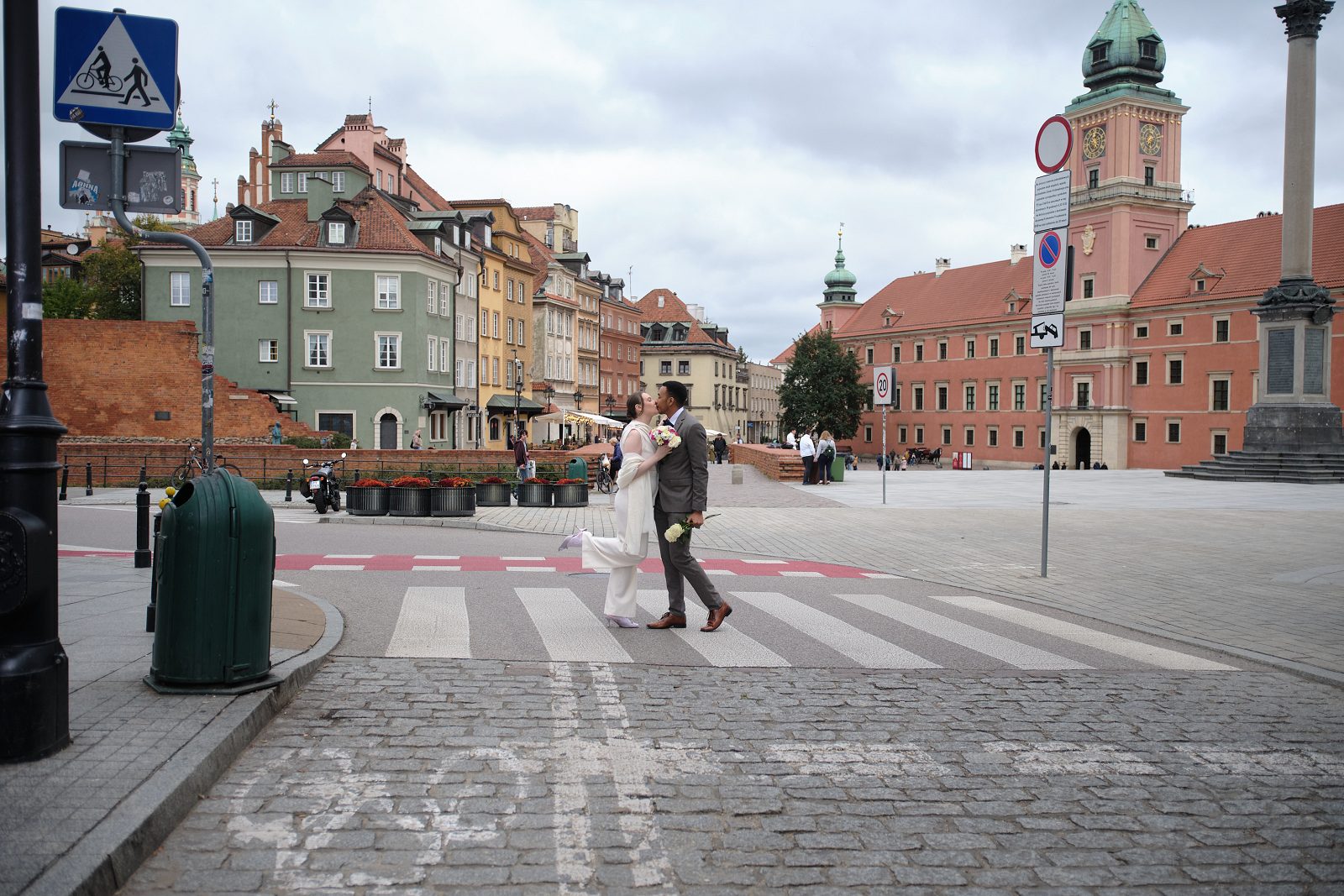 A couple in wedding attire crosses at a pedestrian crossing in Warsaw Old Town.