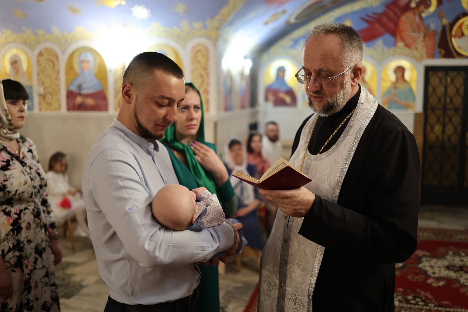 Priest praying over an infant held by a man