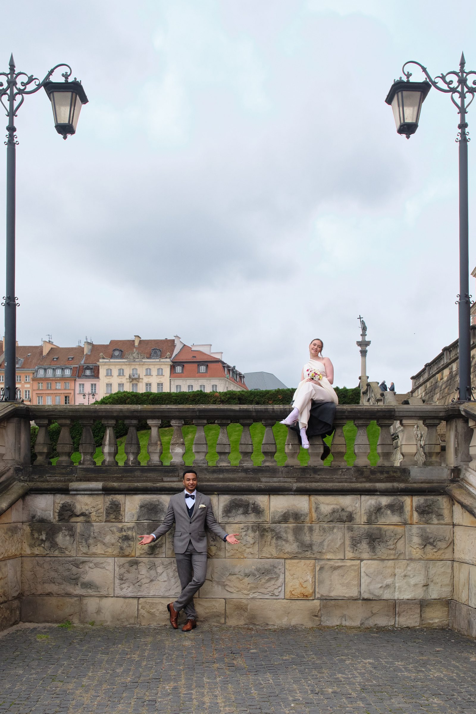 The couple pose by a stone wall, with the bride on the parapet and the groom below.