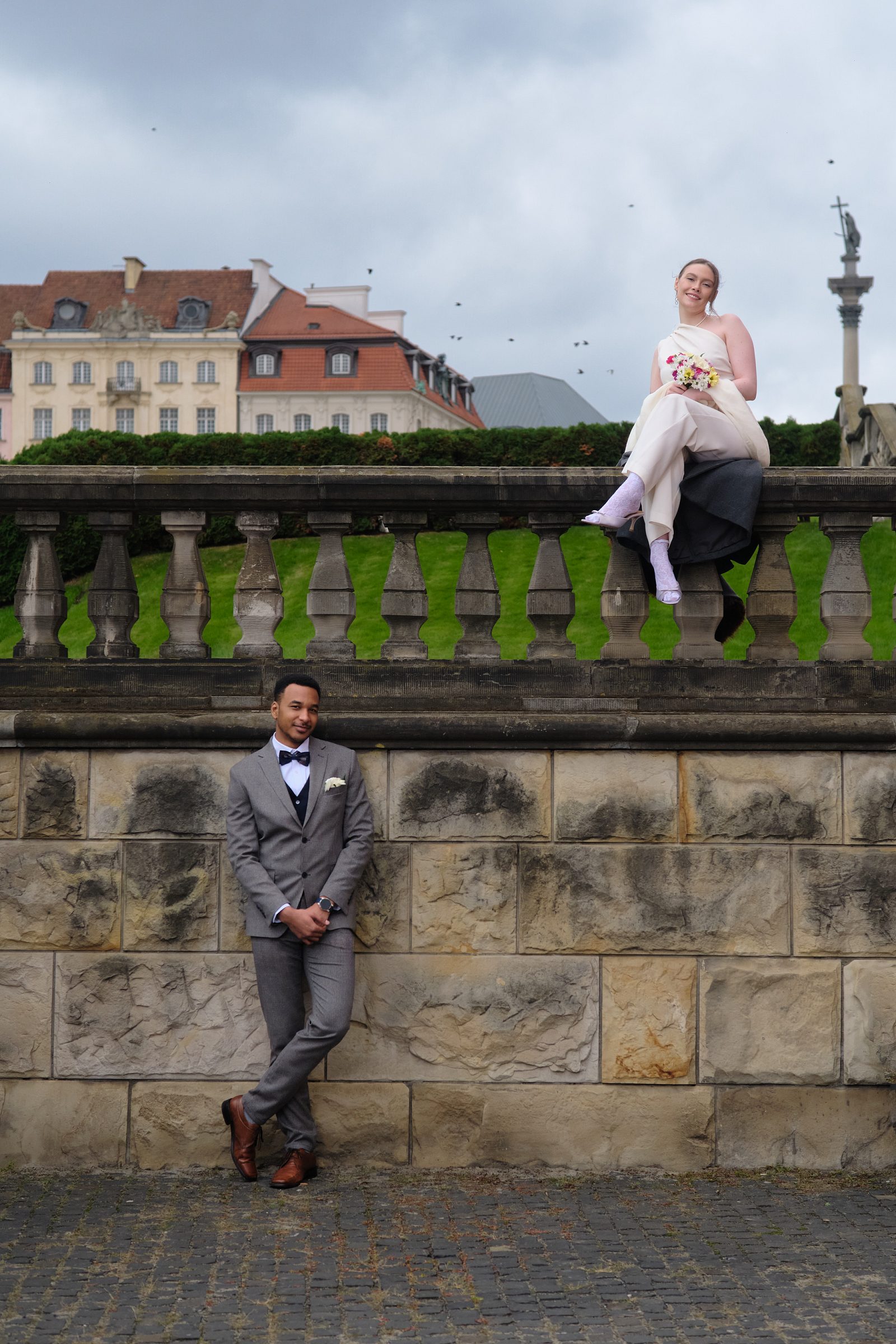 The bride and groom pose at different levels beside a tall stone balustrade.