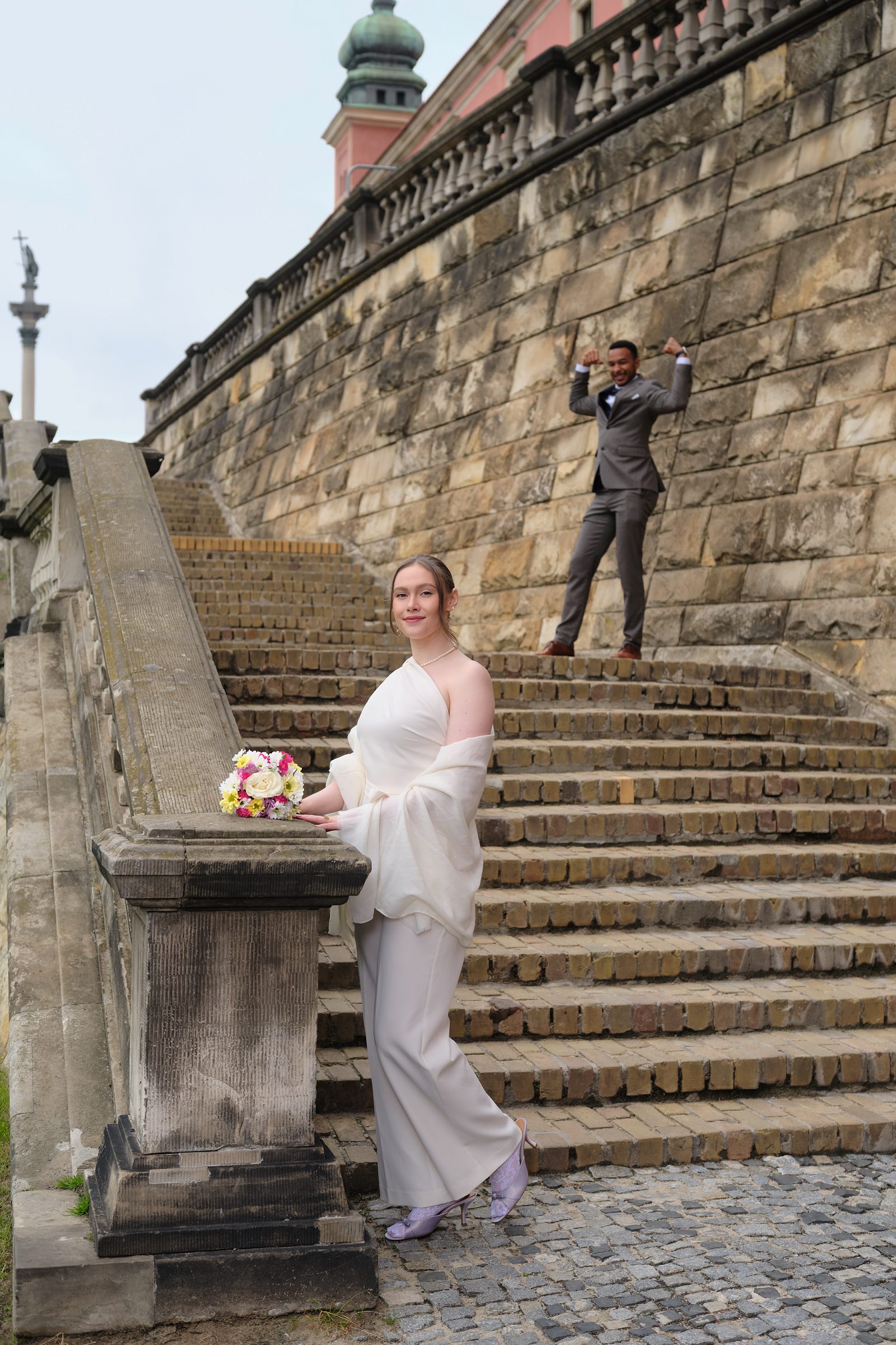 The bride stands beside a stone pedestal with broad steps rising behind her.