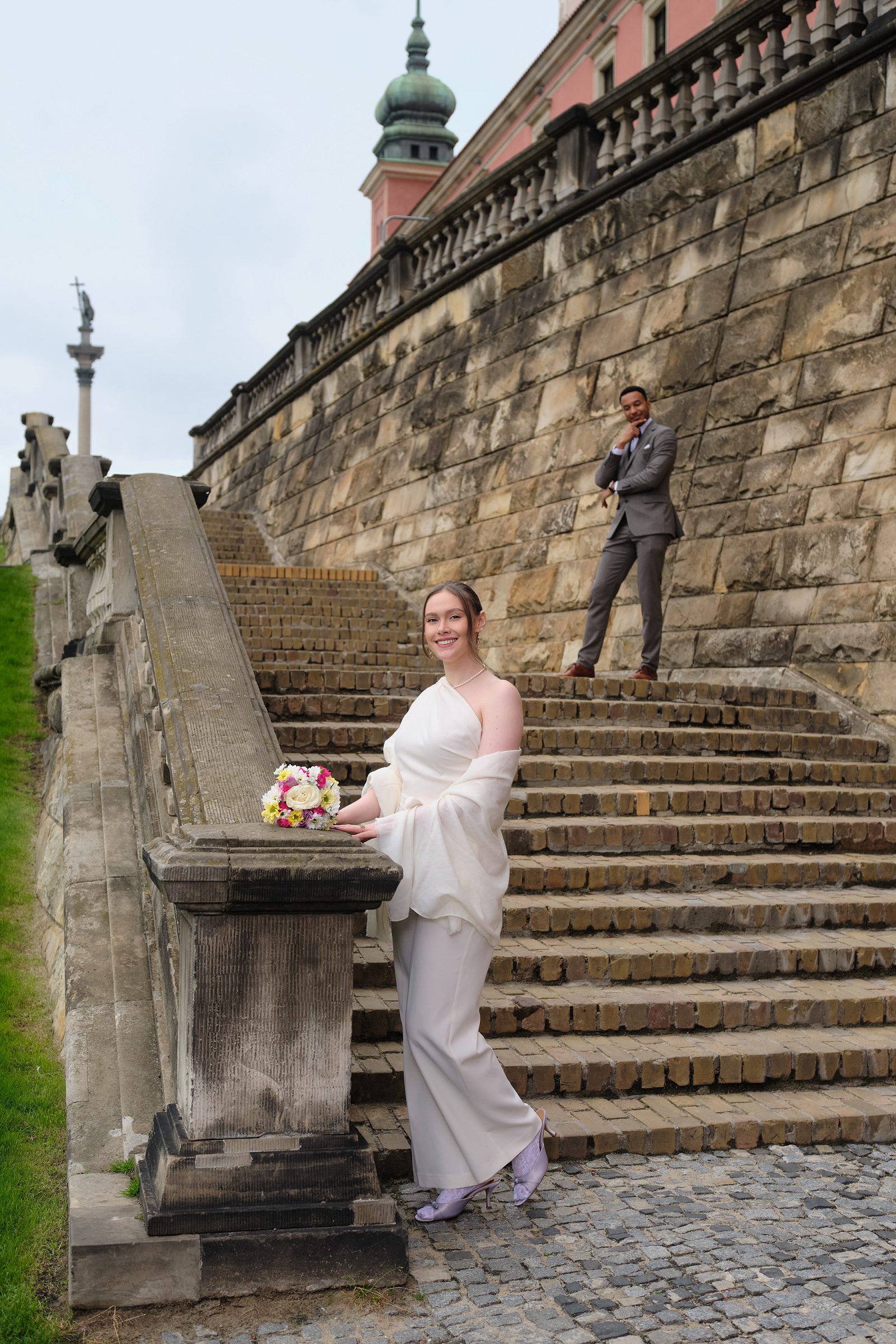 The bride holds her bouquet by a stone balustrade with stairs behind her.