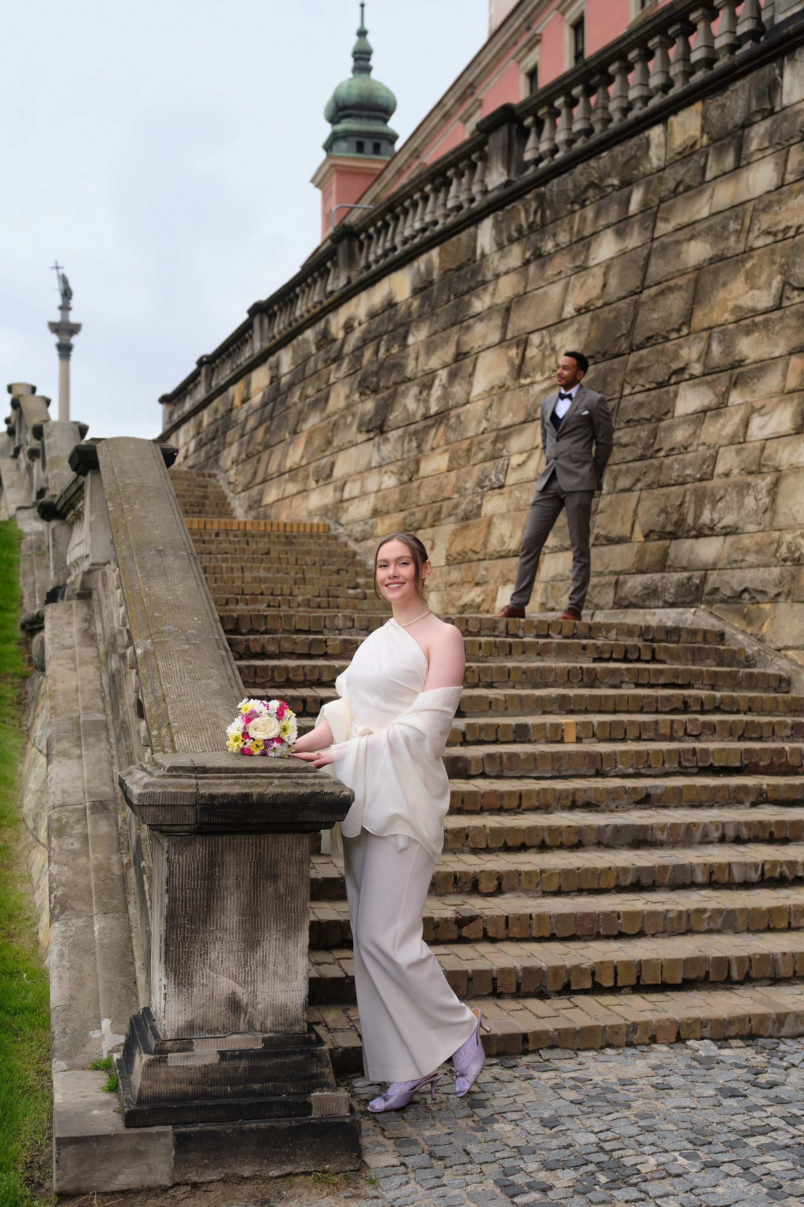 The bride poses beside a stone balustrade near a broad staircase.