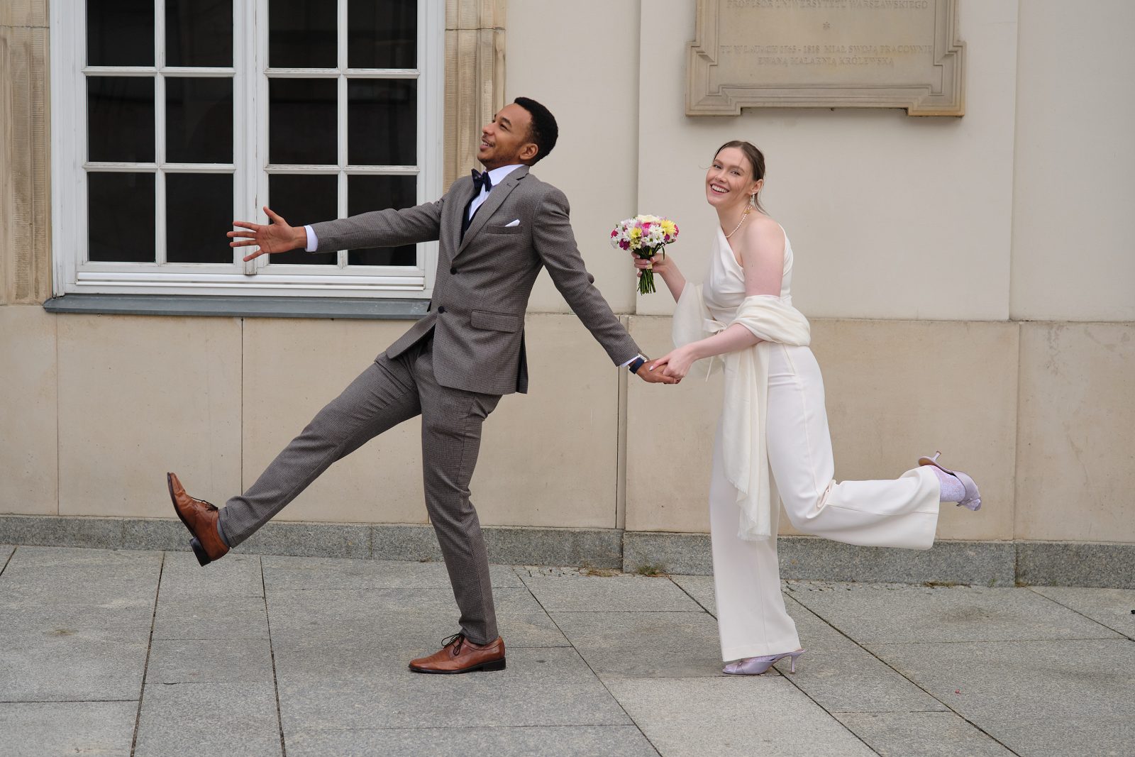 The bride and groom take a wide step toward each other on a cobbled square.