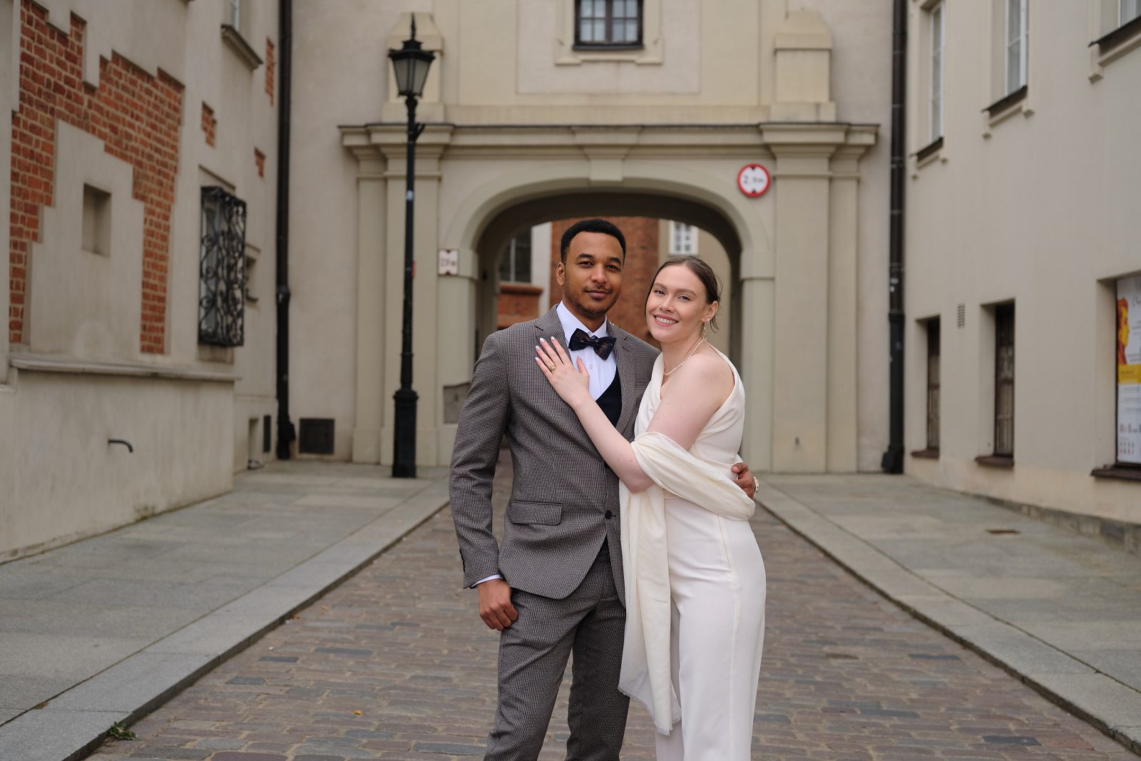 The bride and groom walk along a narrow cobbled street in Warsaw Old Town.