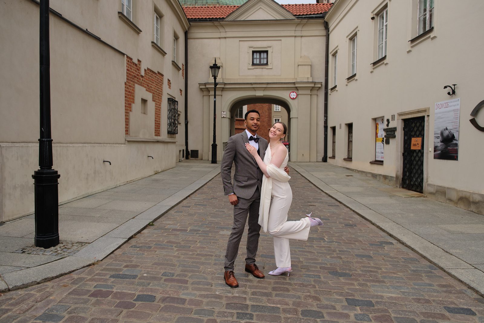 The groom embraces the bride holding a bouquet on a historic city street.