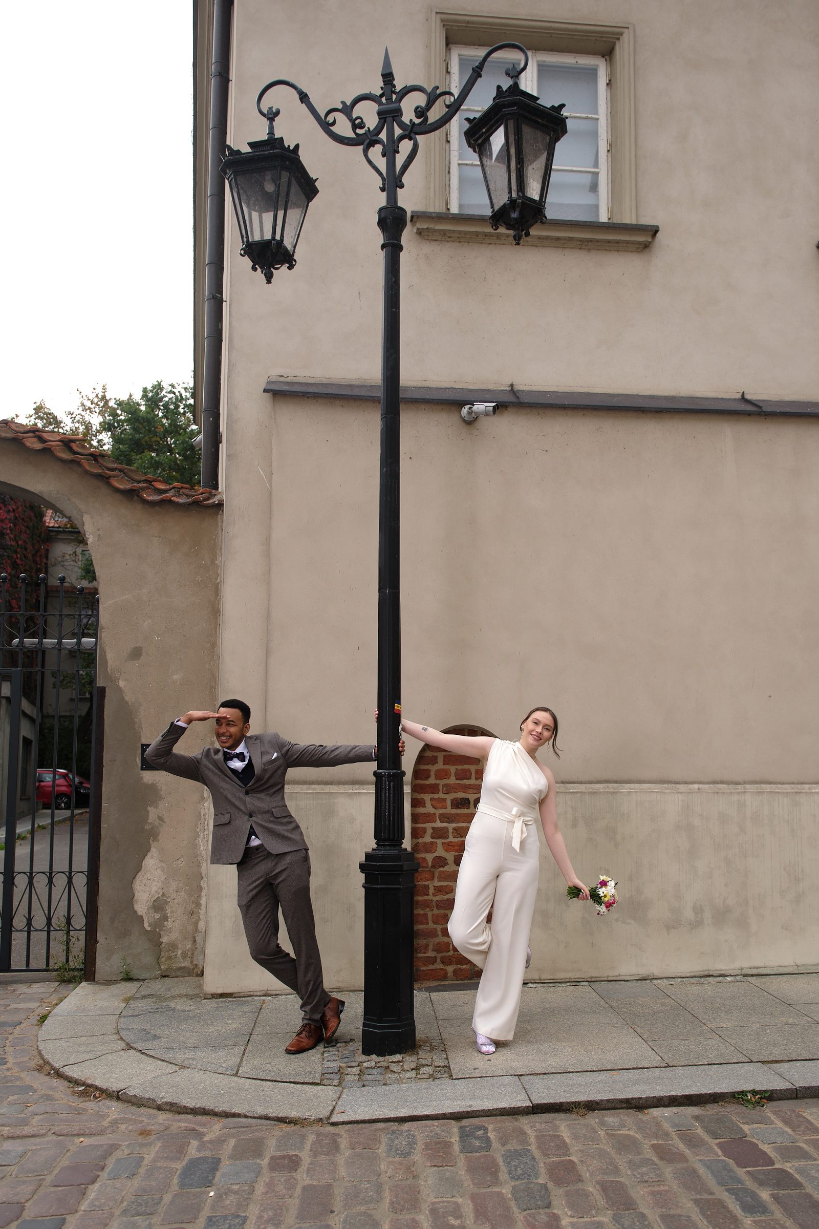 The bride and groom stand on opposite sides of an old street lamp, holding its post.