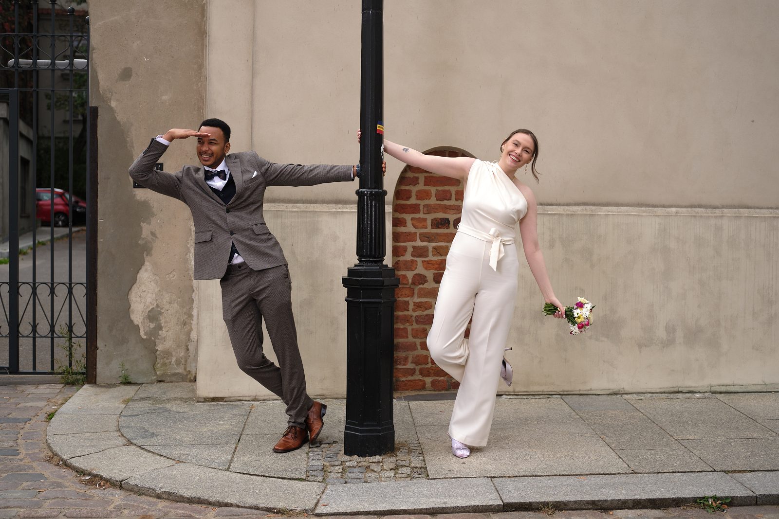 The couple pose by a street lamp, holding its post and extending their free arms.
