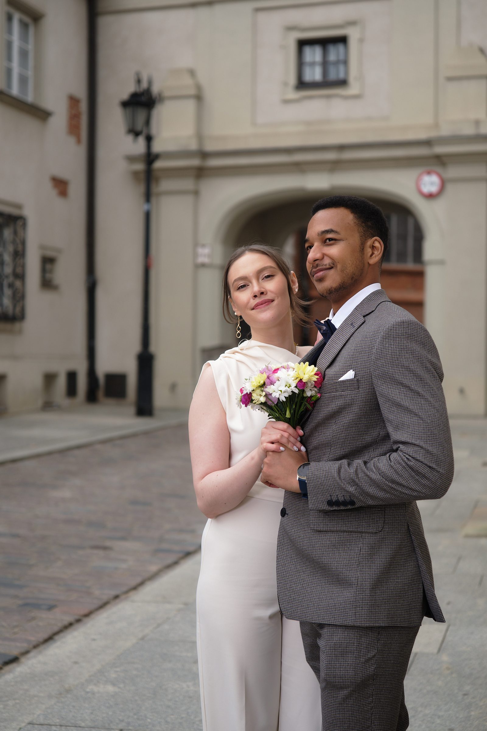 The bride holds her bouquet as the groom embraces her beneath an Old Town arch.