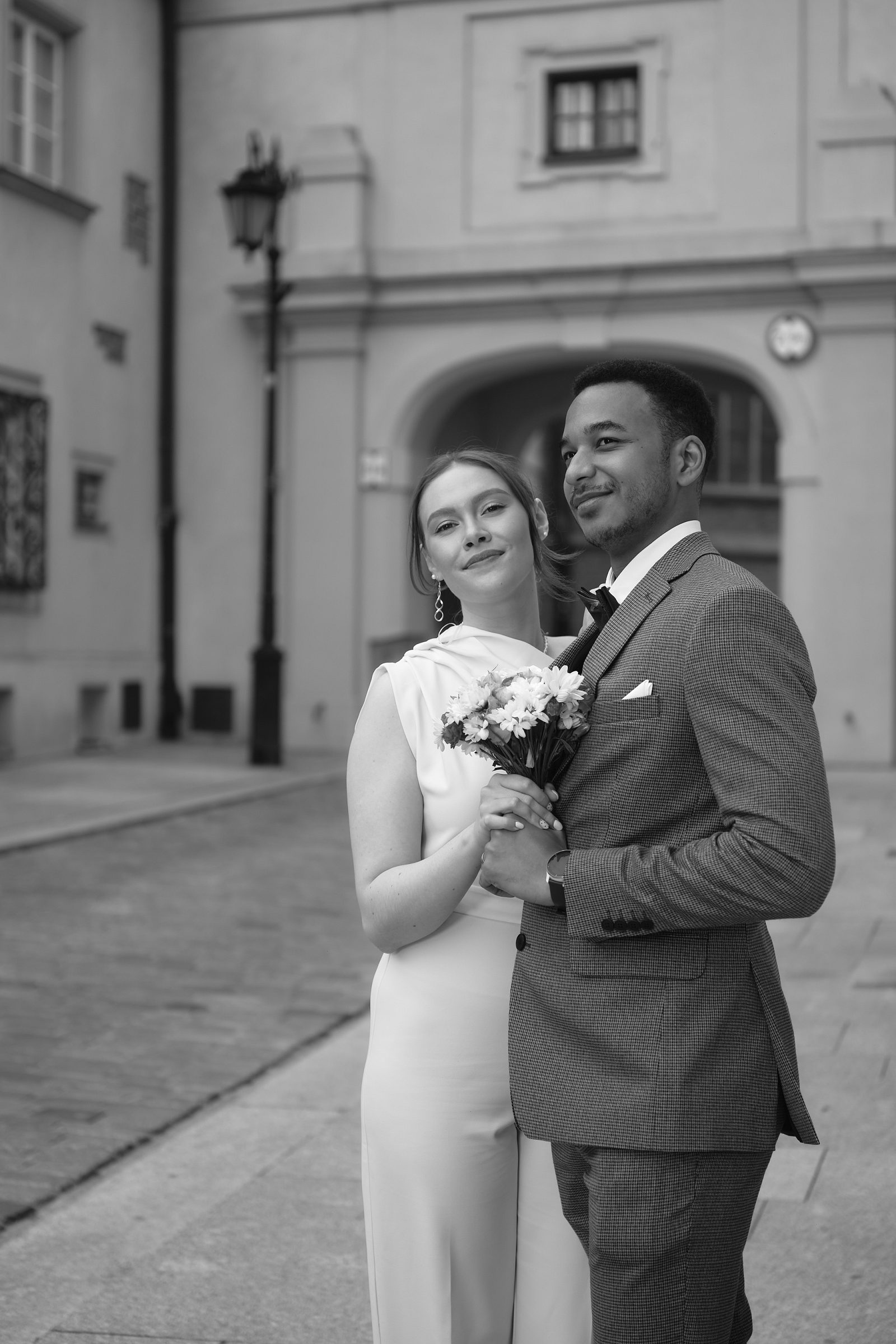 Black-and-white portrait of the bride holding her bouquet in the groom’s arms.