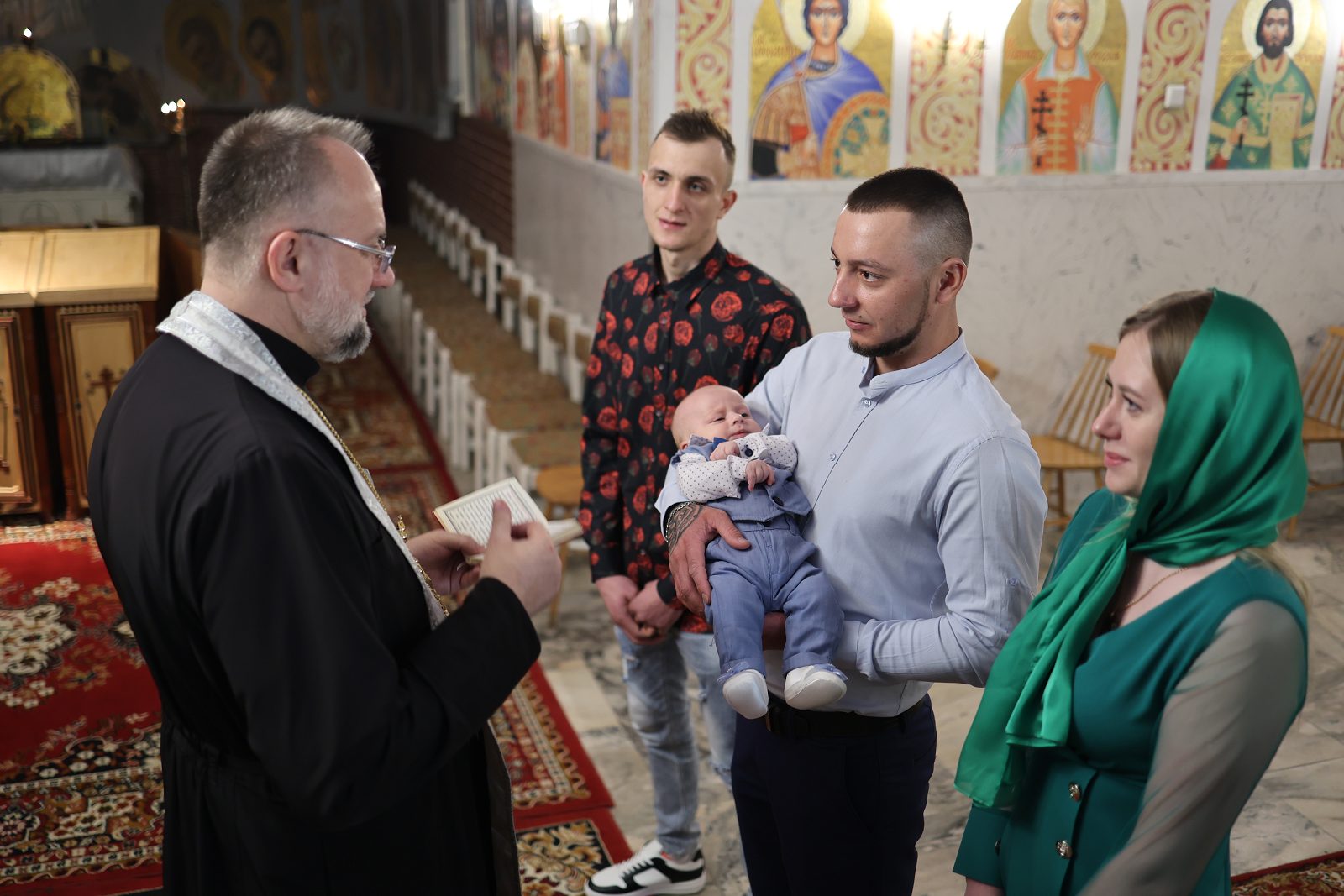 Priest speaking with the family beside the infant during baptism