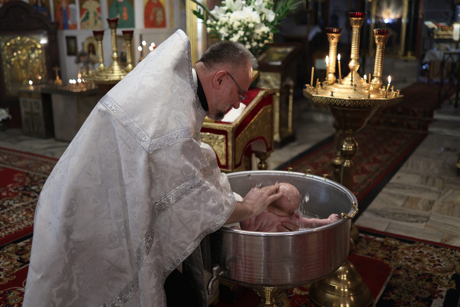 Priest lowering an infant into the baptismal font