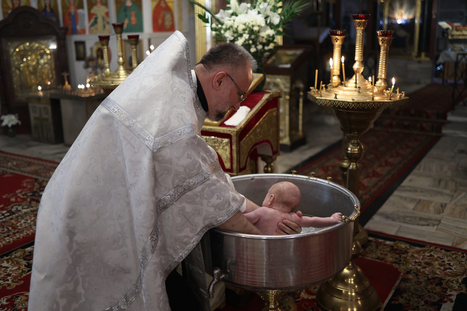 Priest holding an infant above the baptismal font