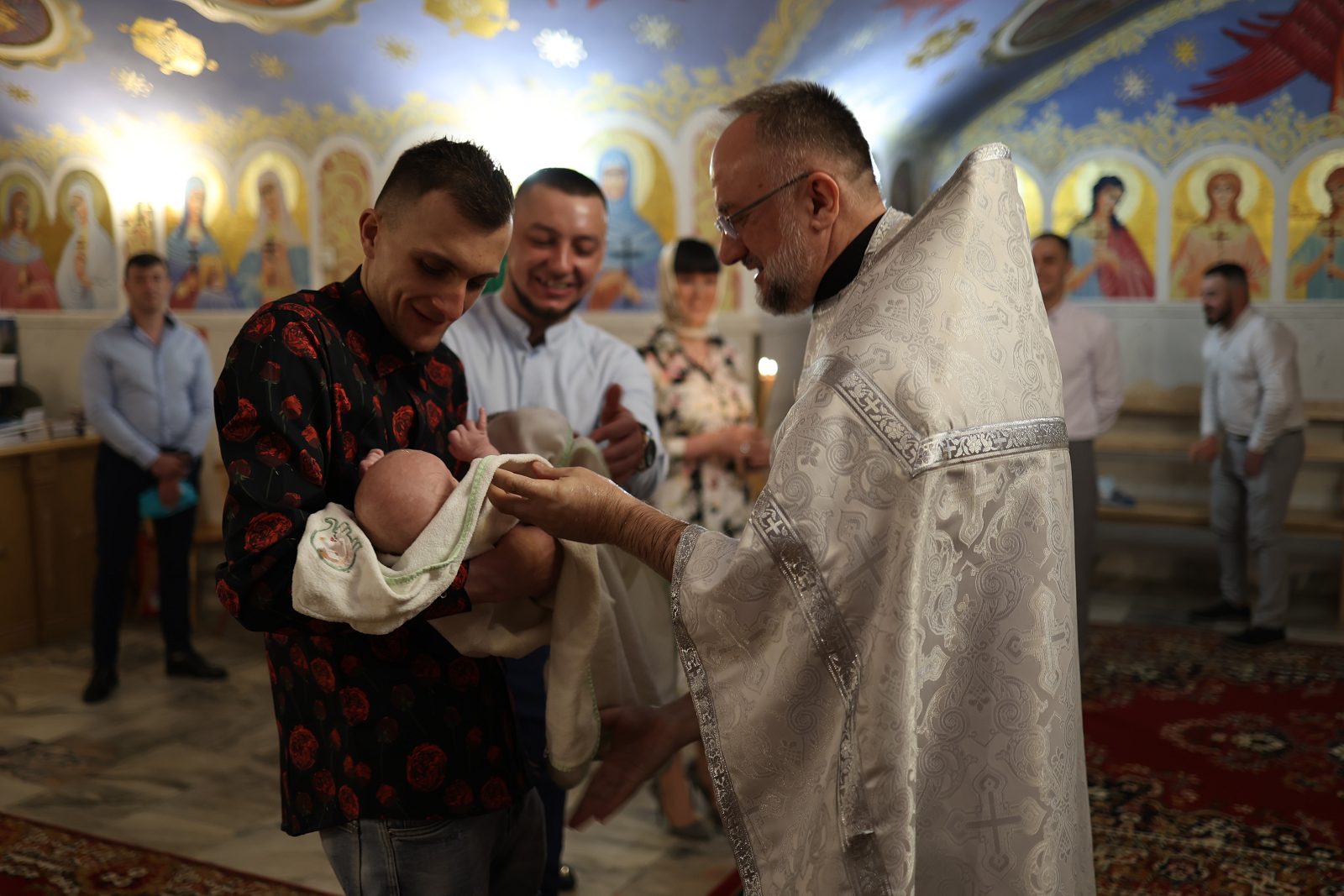 Man holding baptism clothing beside the priest
