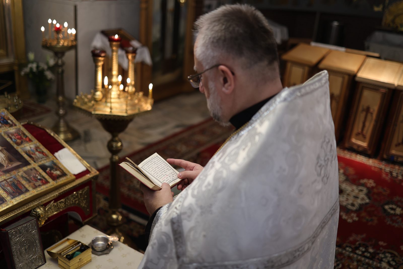 Priest reading a prayer by an icon and candle stand