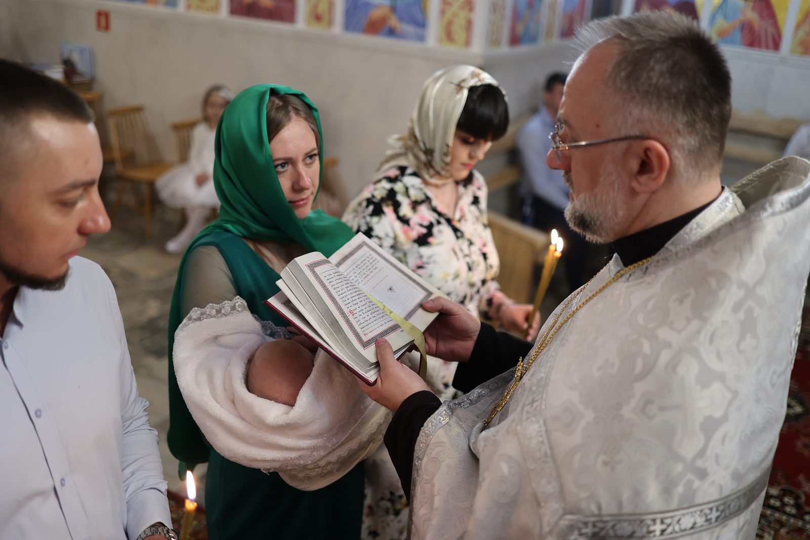 Priest praying over an infant held by a woman