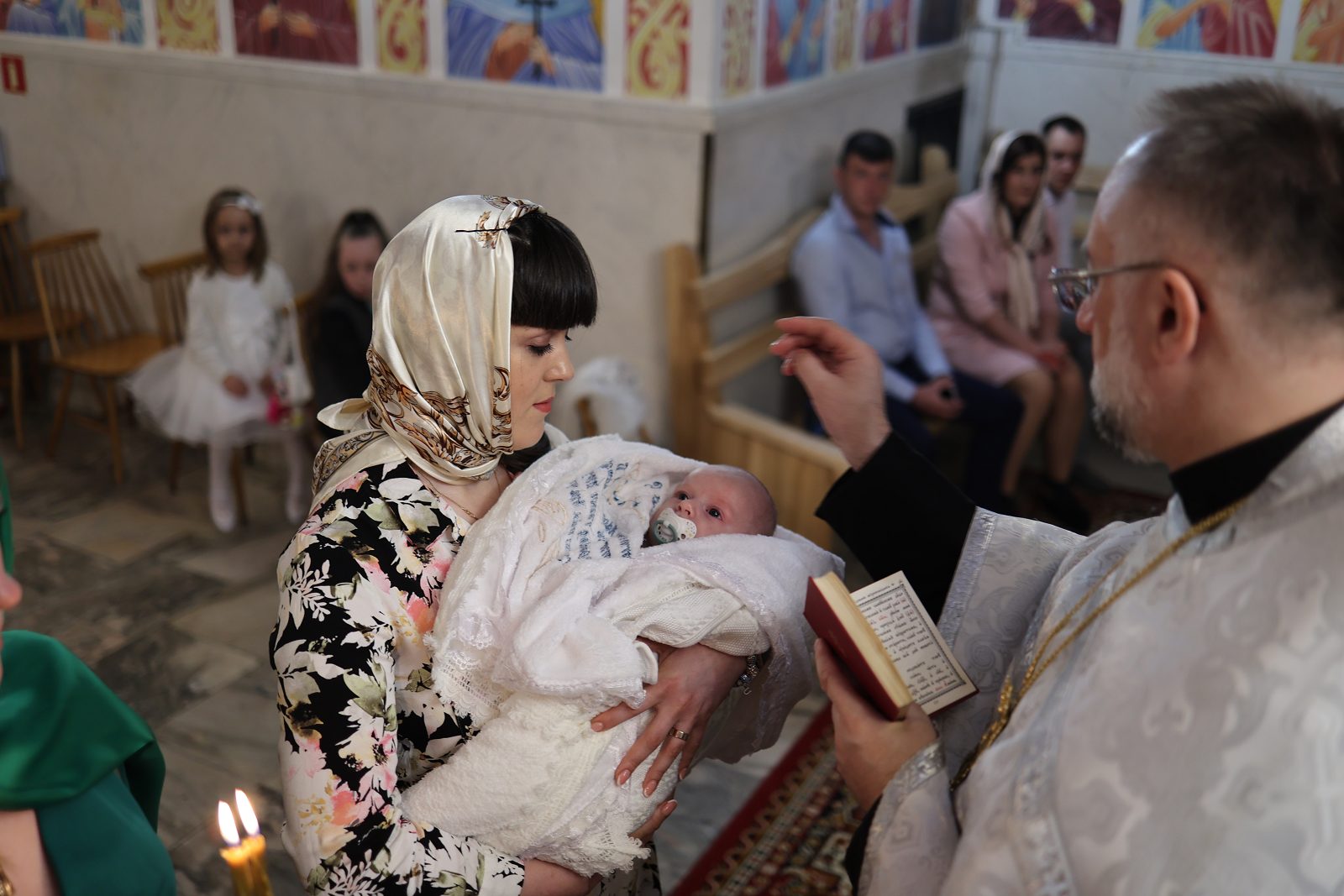 Priest praying over an infant held by a woman