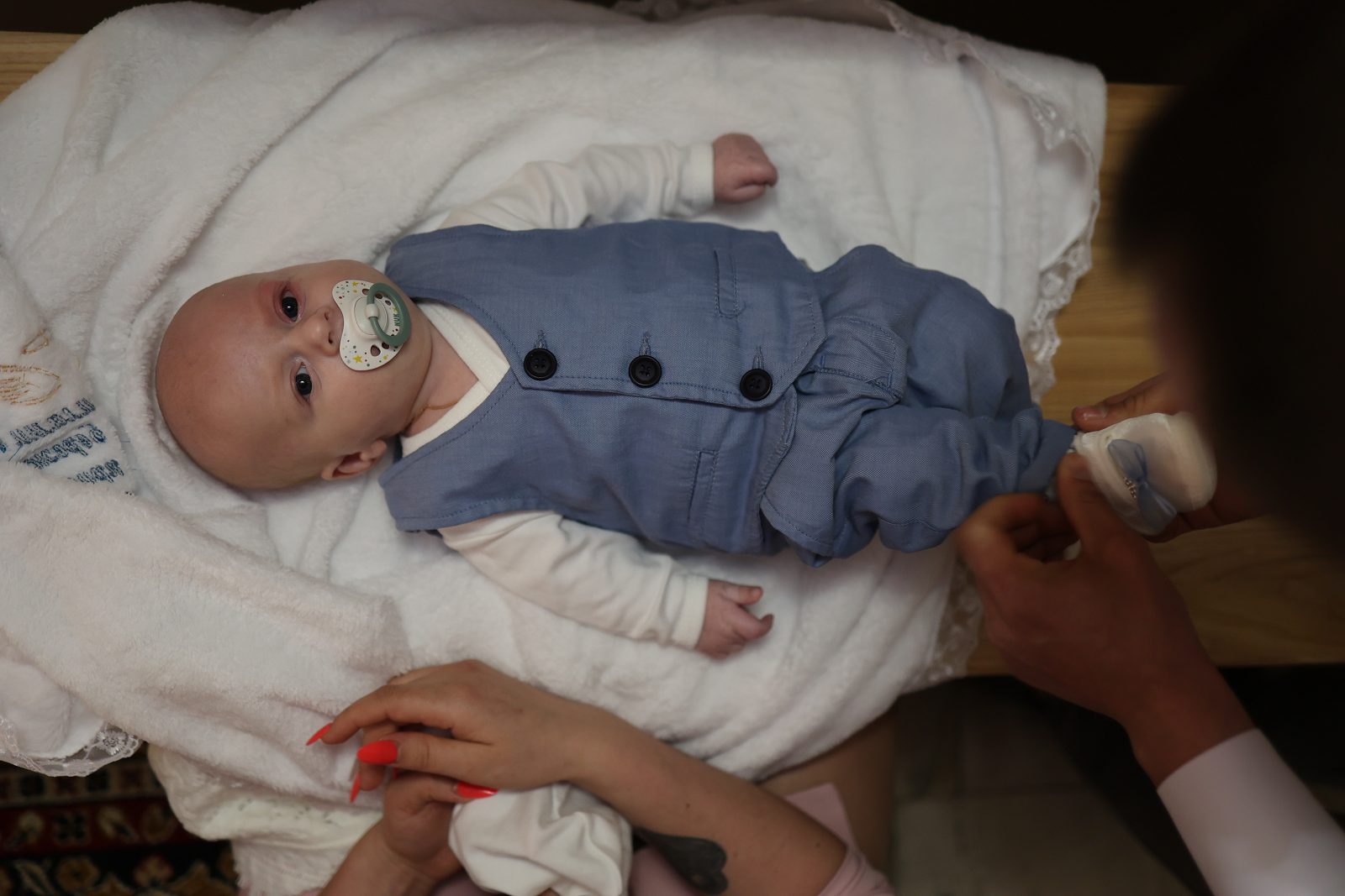 Infant in a blue outfit lying on a baptism pillow