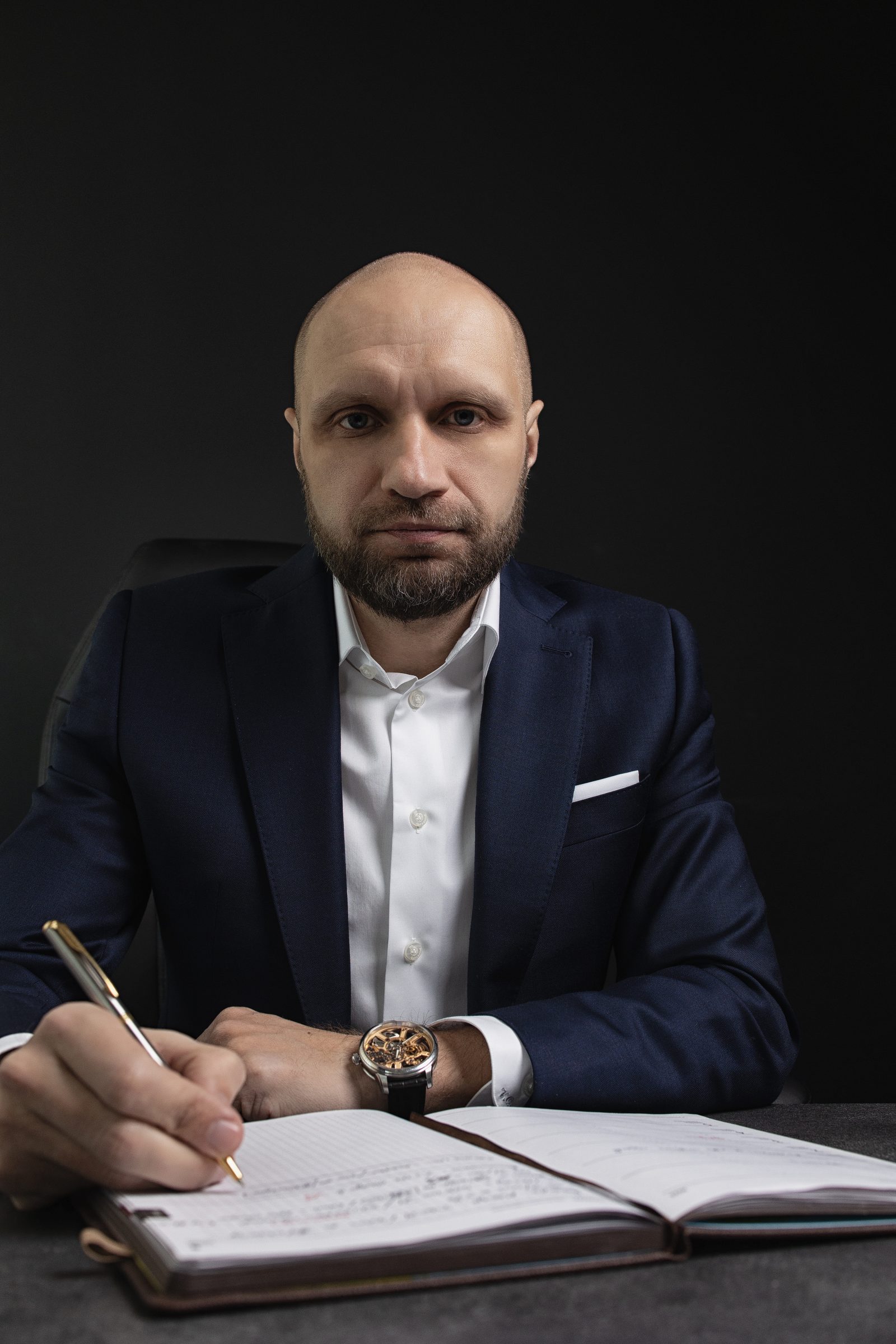 Mężczyzna w granatowym garniturze robi notatkę w notesie