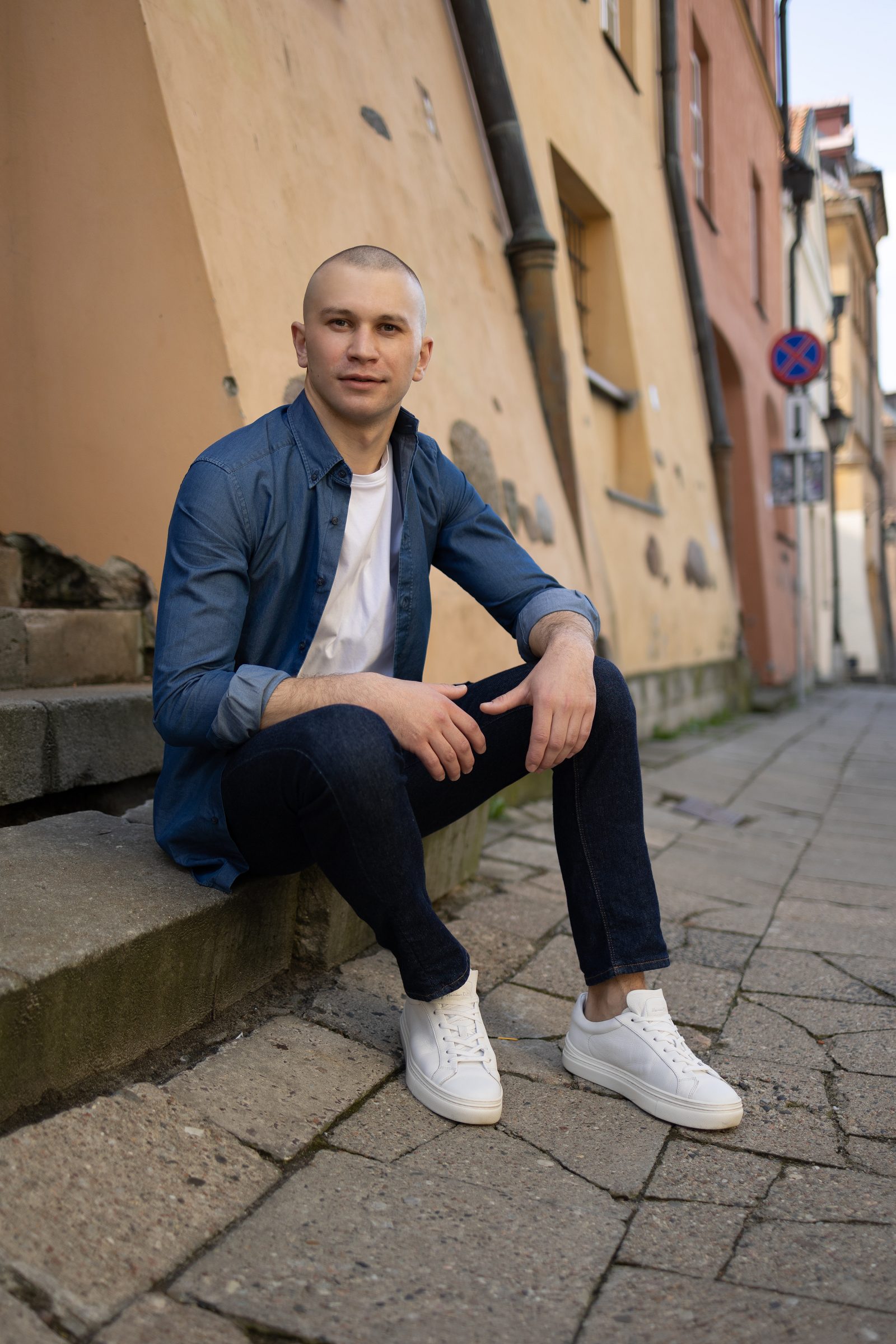 Mężczyzna w niebieskiej koszuli siedzi przy ścianie na miejskiej ulicy