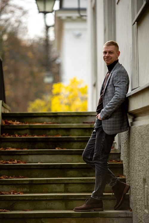 Mężczyzna w kraciastej marynarce stoi na schodach przy budynku