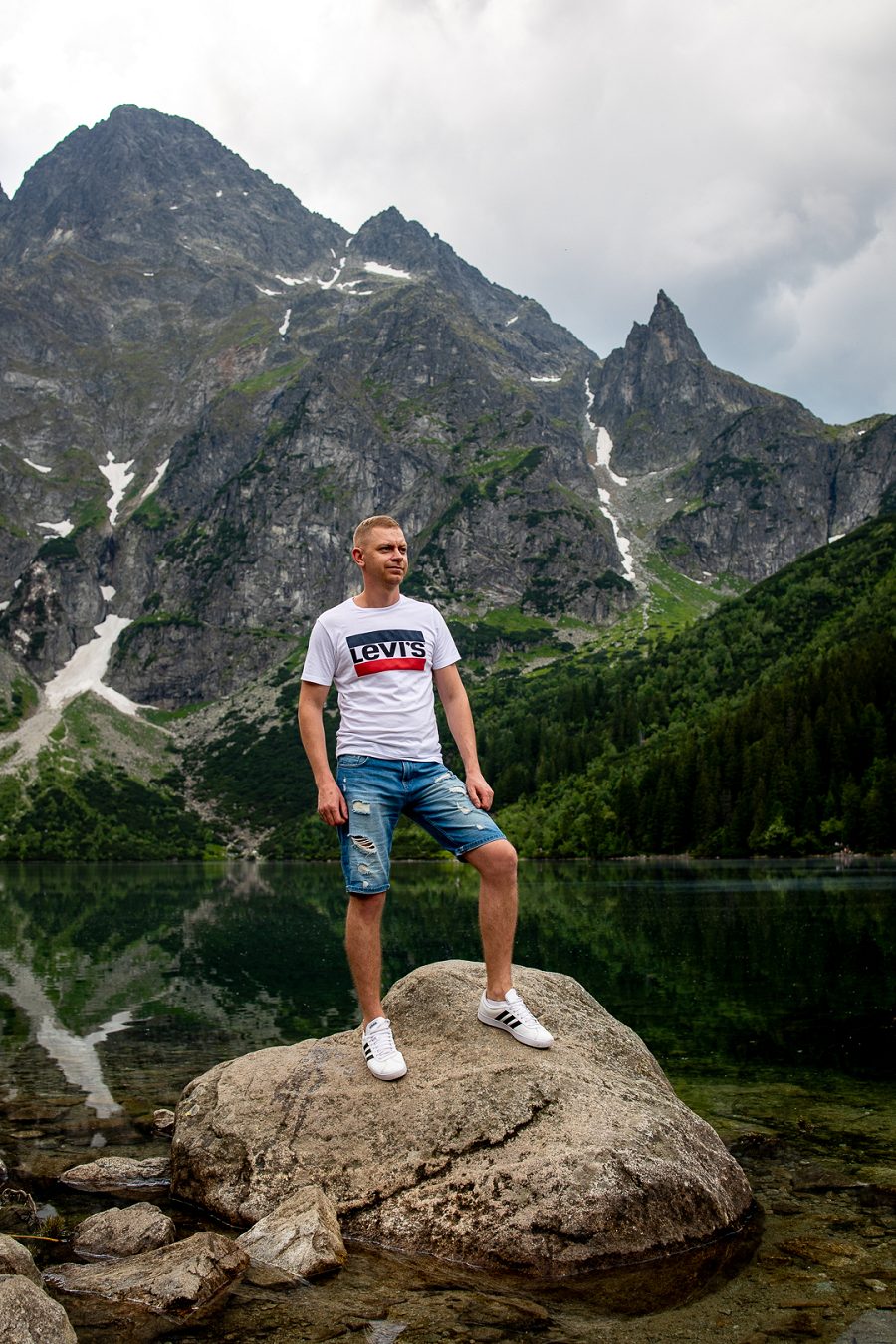 Mężczyzna stoi na skale przy górskim jeziorze