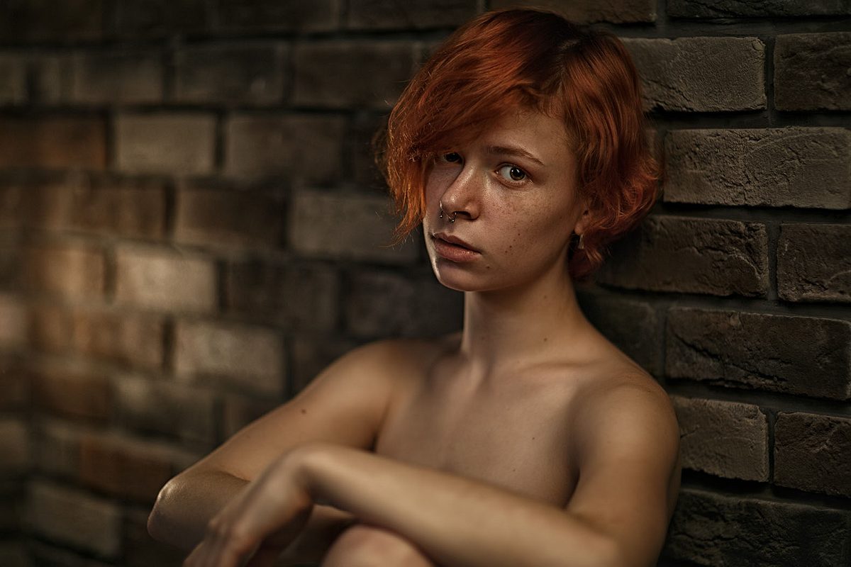 Portrait of a red-haired woman beside a brick wall