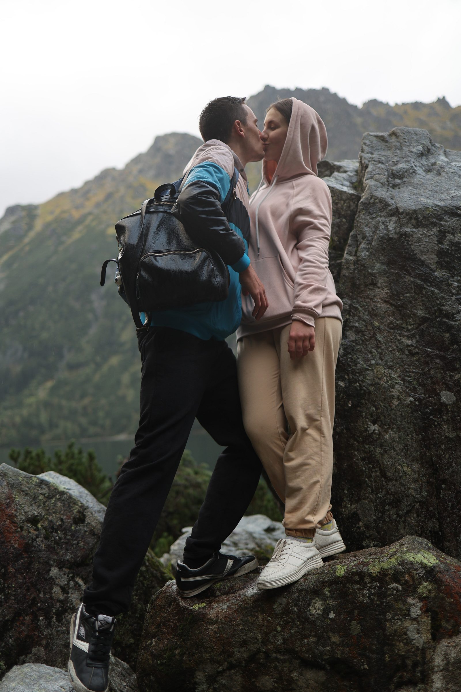Man kissing a woman on a rock in the mountains