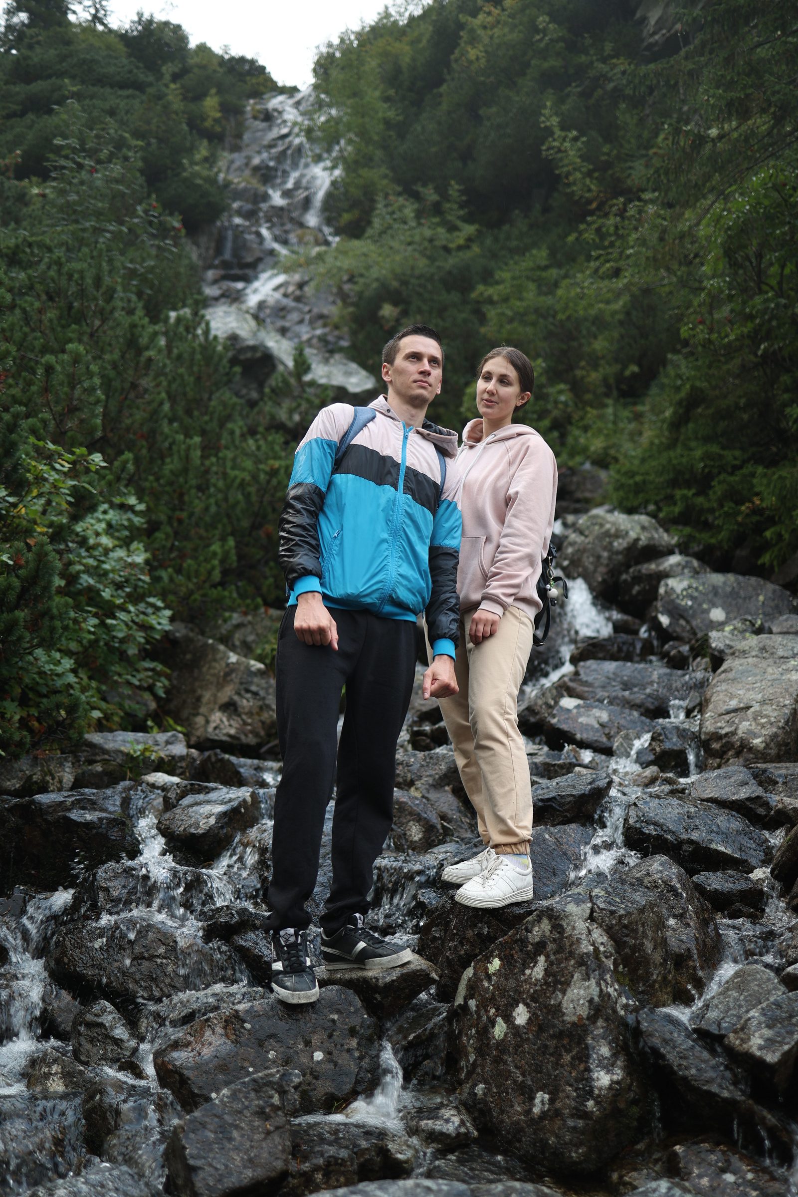 Couple standing on rocks beside a mountain waterfall