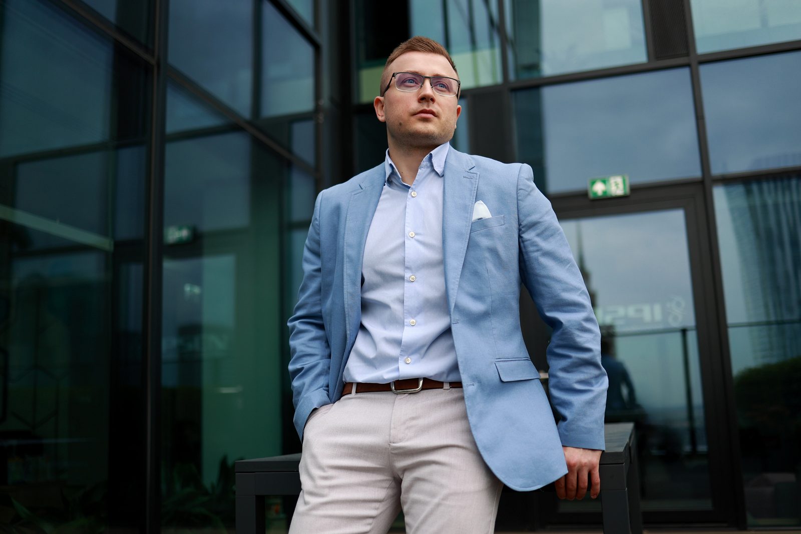 Чоловік у блакитному піджаку біля входу до сучасної будівлі