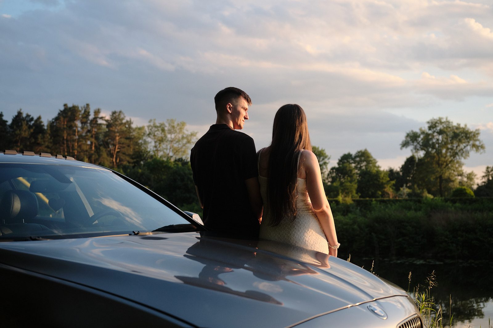 Couple standing beside a car against the setting sun and water