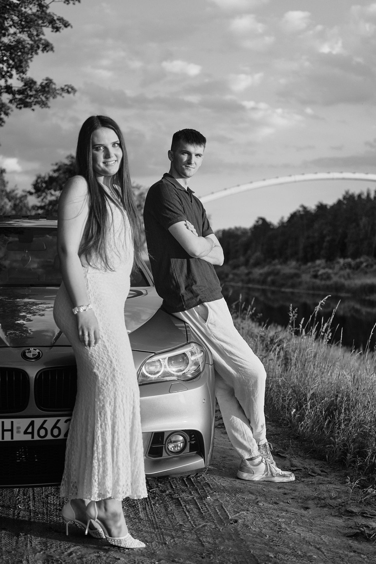 Black-and-white portrait of a couple beside a car by the water