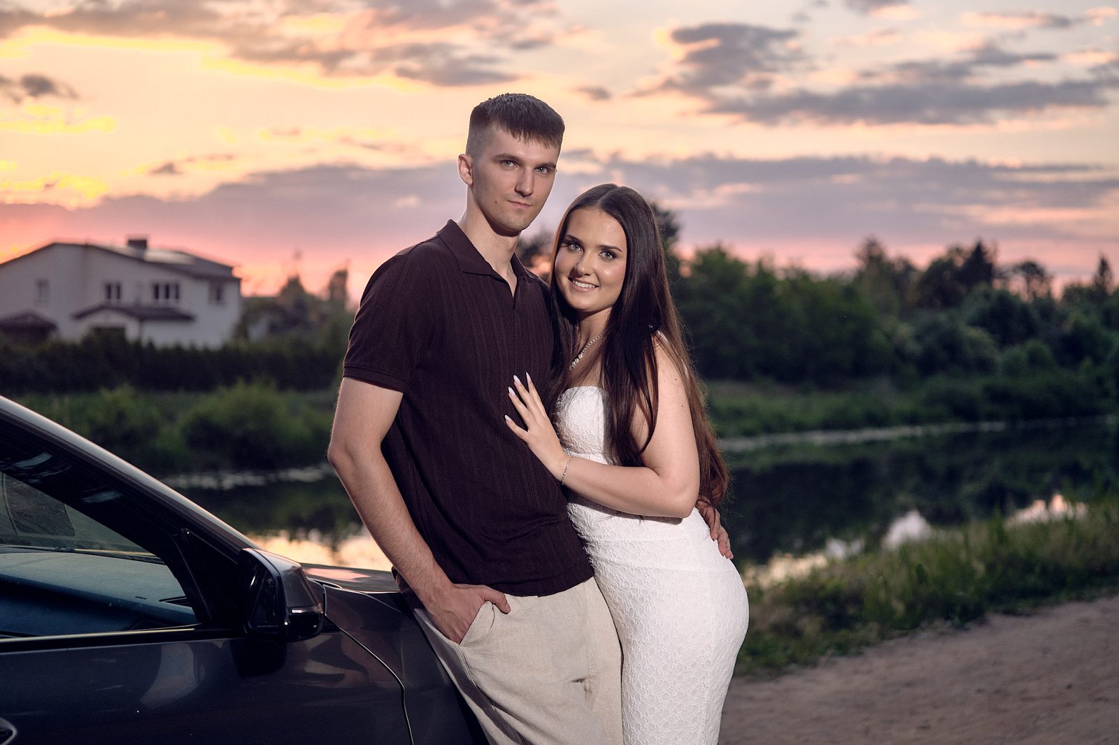 Portrait of a couple beside a car against the evening sky