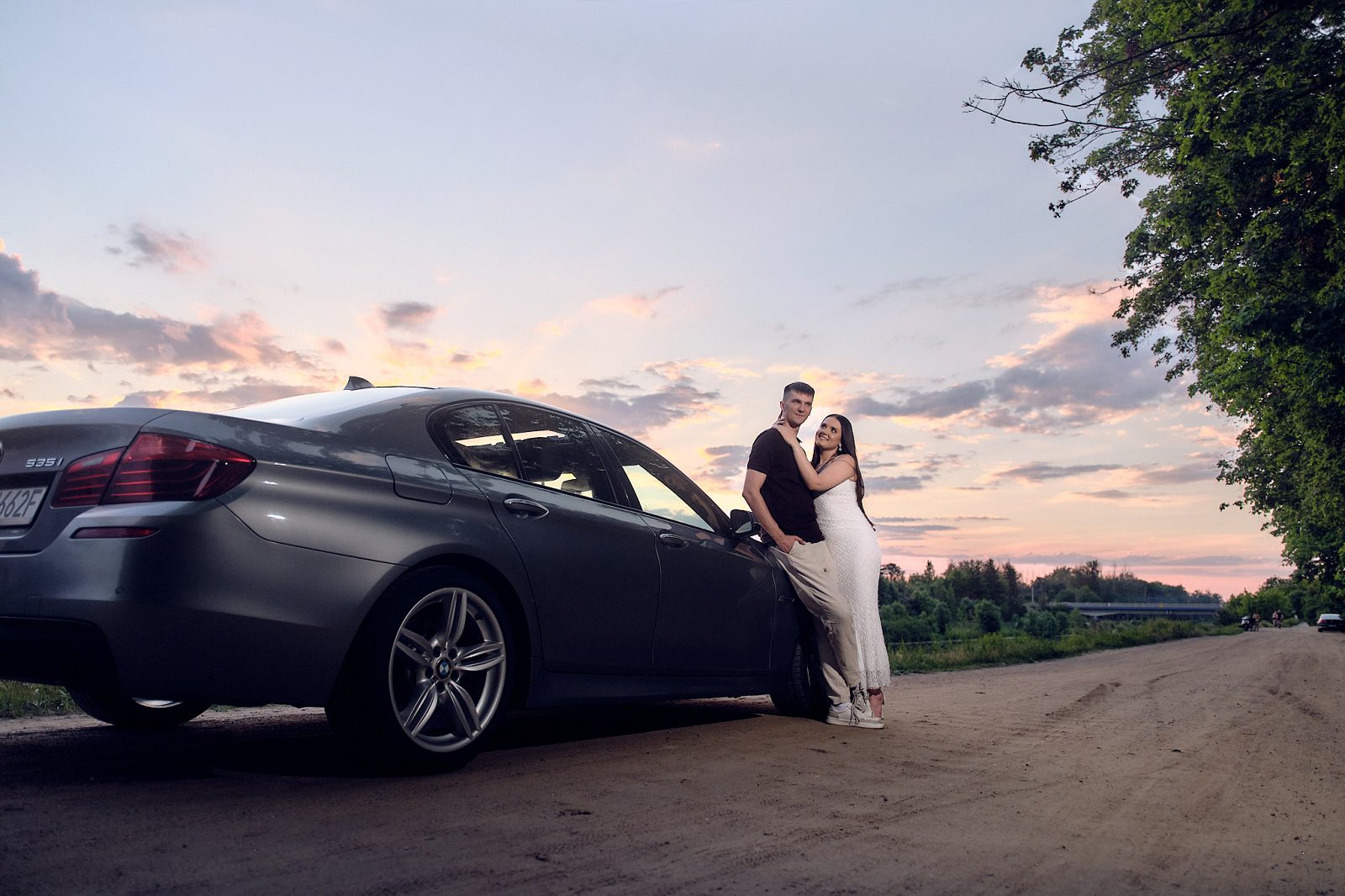 Couple standing beside a car on a dirt road by the water in the evening light