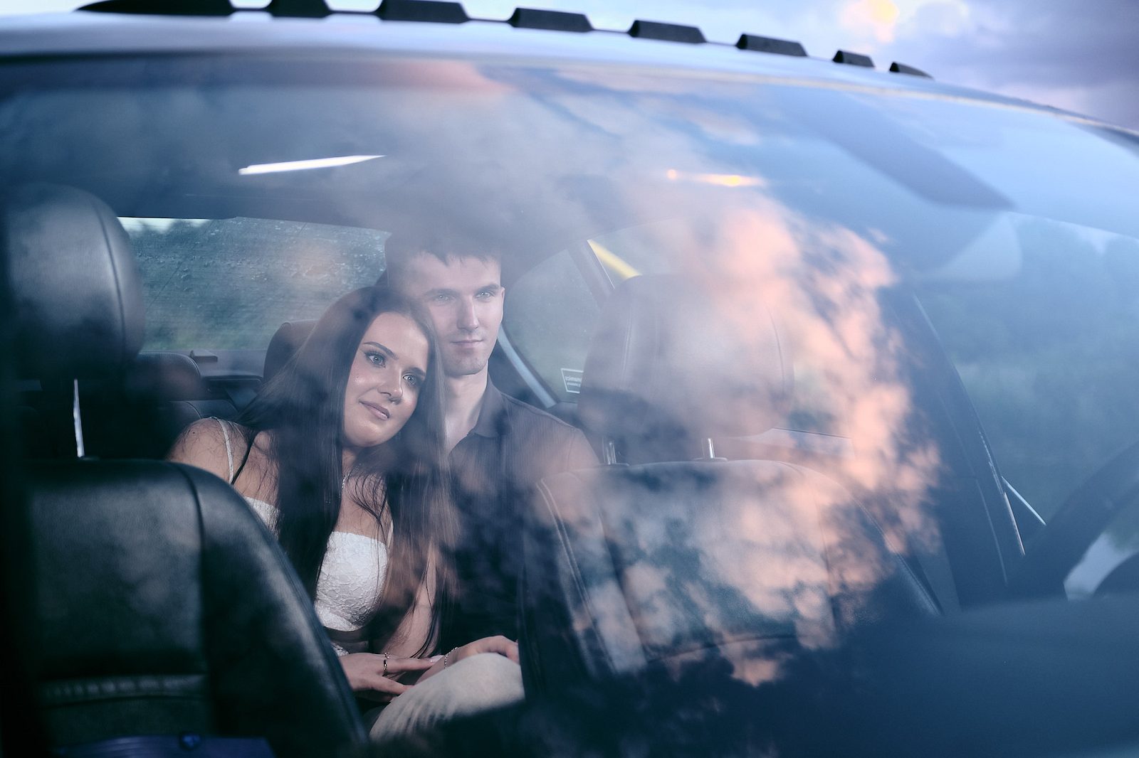 Couple inside a car photographed through the windshield with clouds reflected in the glass