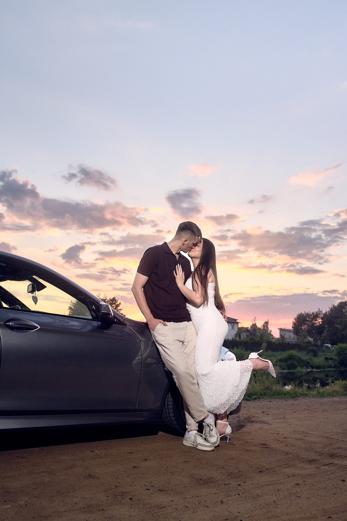 Couple kissing beside a car against the evening sky