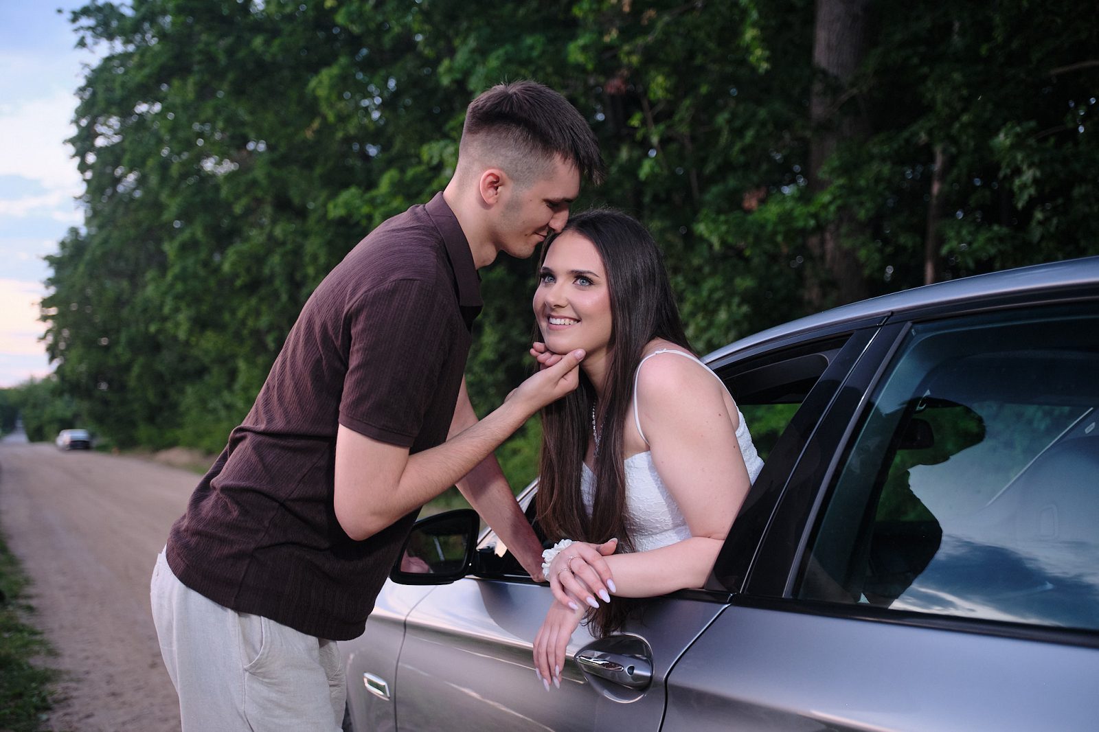 Man touching a woman’s chin beside a car on a forest road