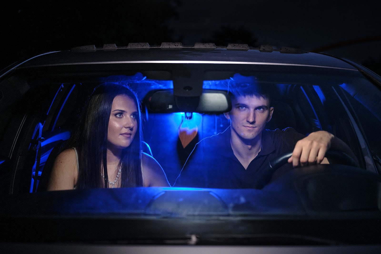 Couple inside a car in blue light; the man is driving and the woman sits beside him