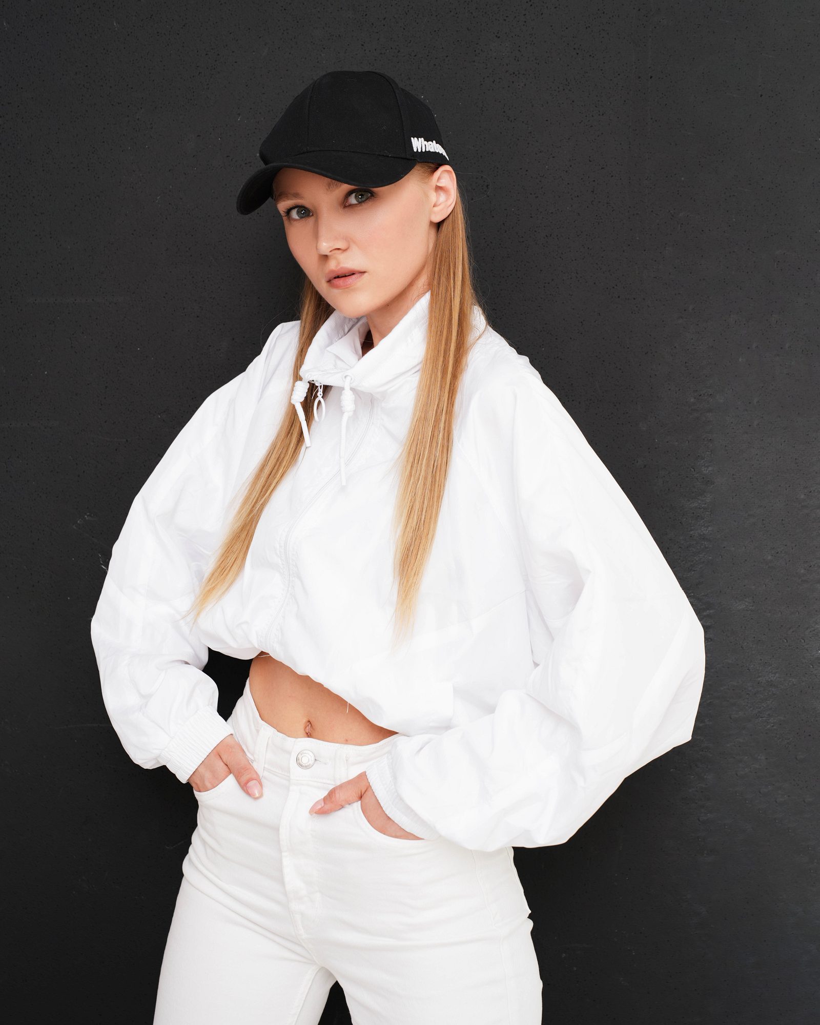 Woman in a white jacket and black cap against a dark background