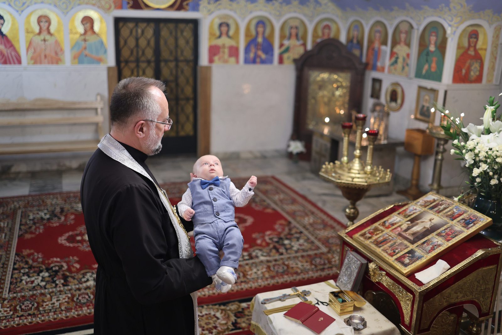 Священник тримає немовля біля аналоя під час хрещення