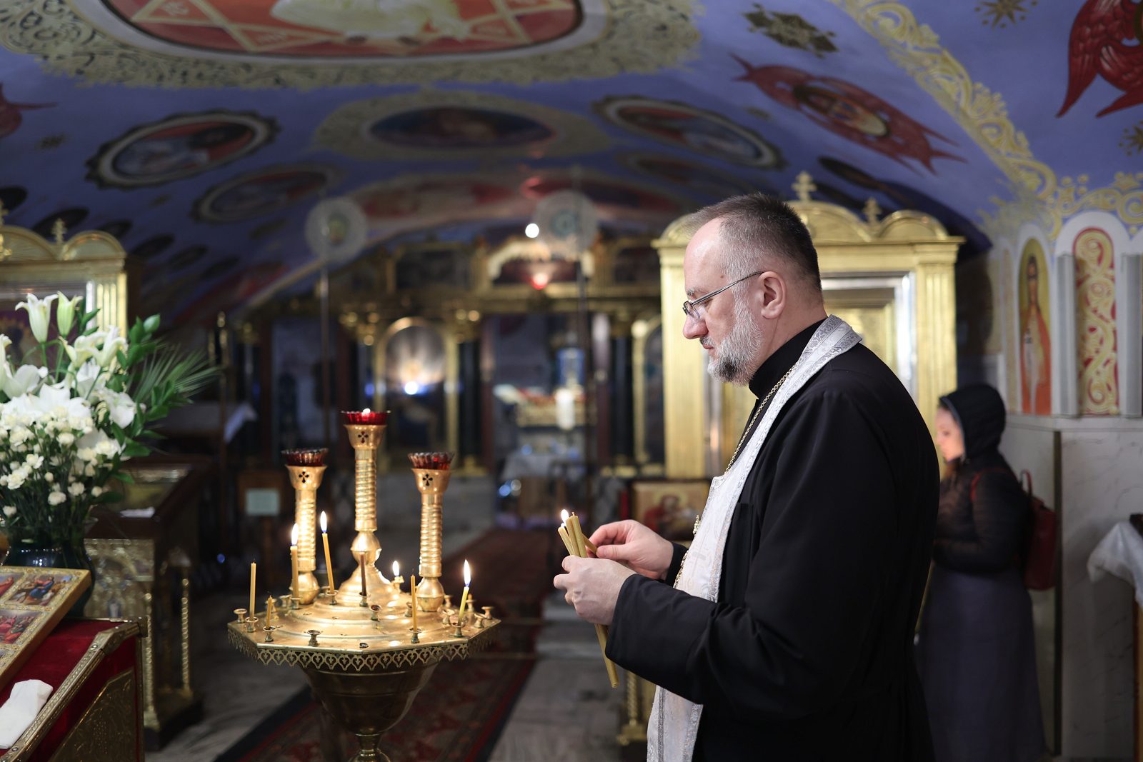 Священник запалює свічку біля свічника в храмі