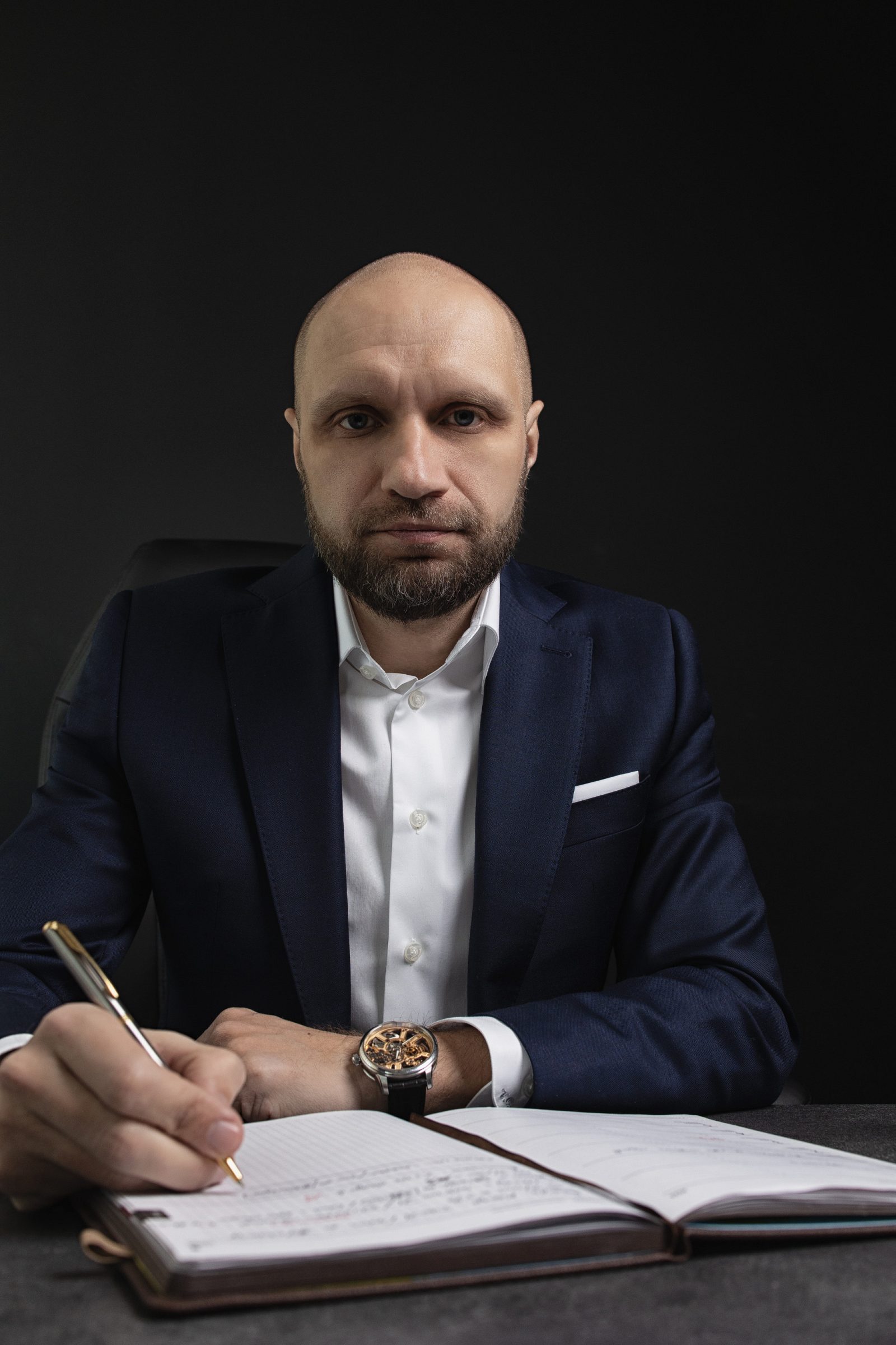 Man in a navy suit making a note in a notebook