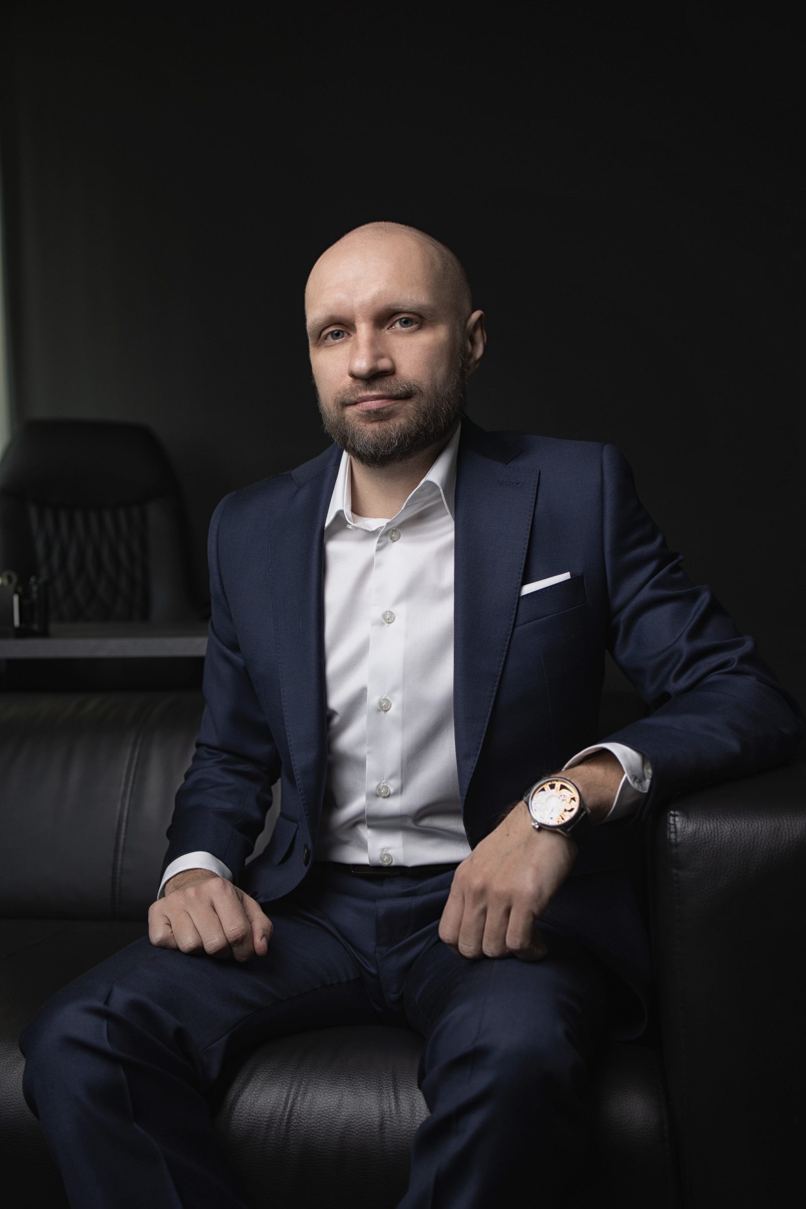 Man in a navy suit seated in an office chair