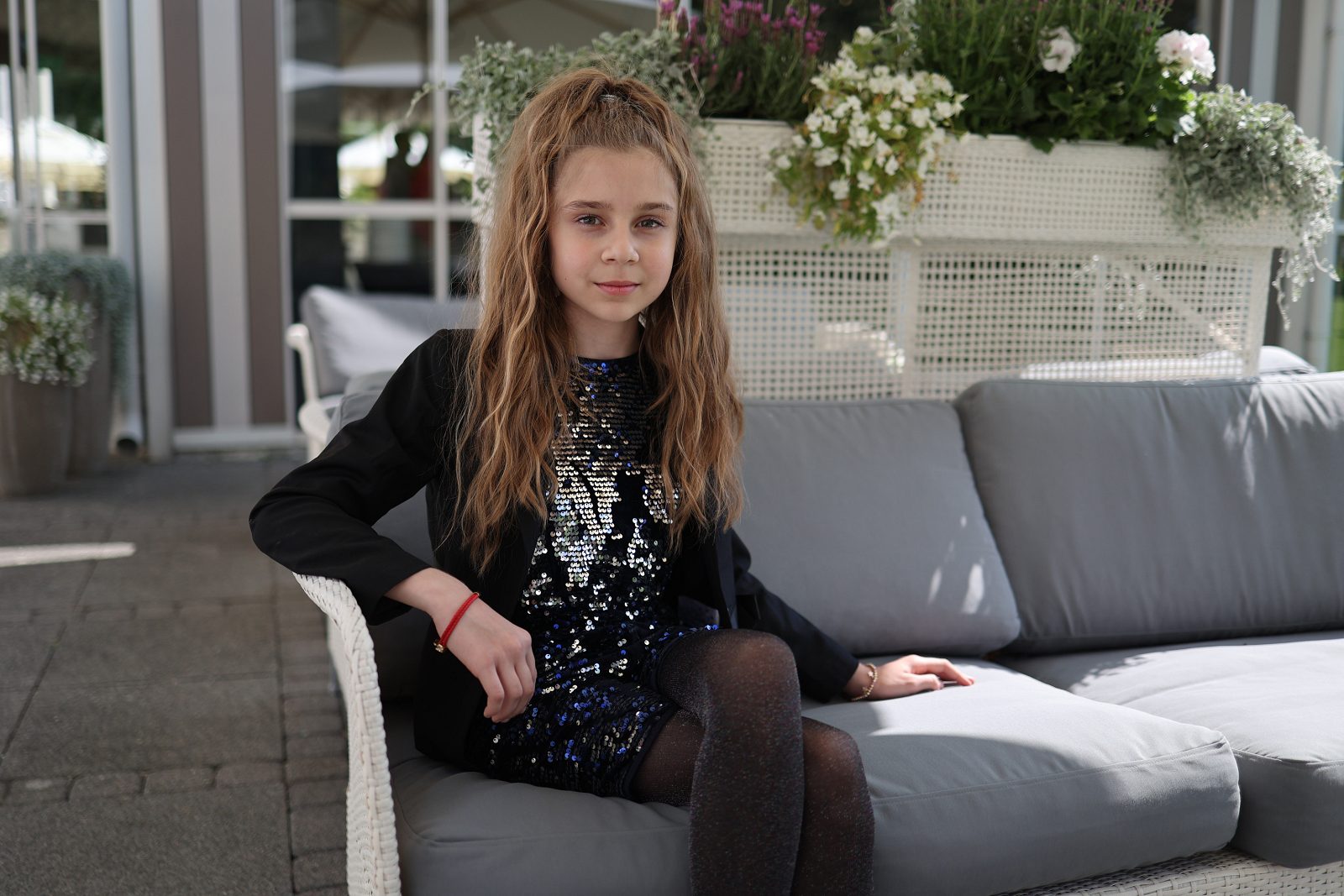 Dziewczynka w czarnej sukience z cekinami siedzi na sofie