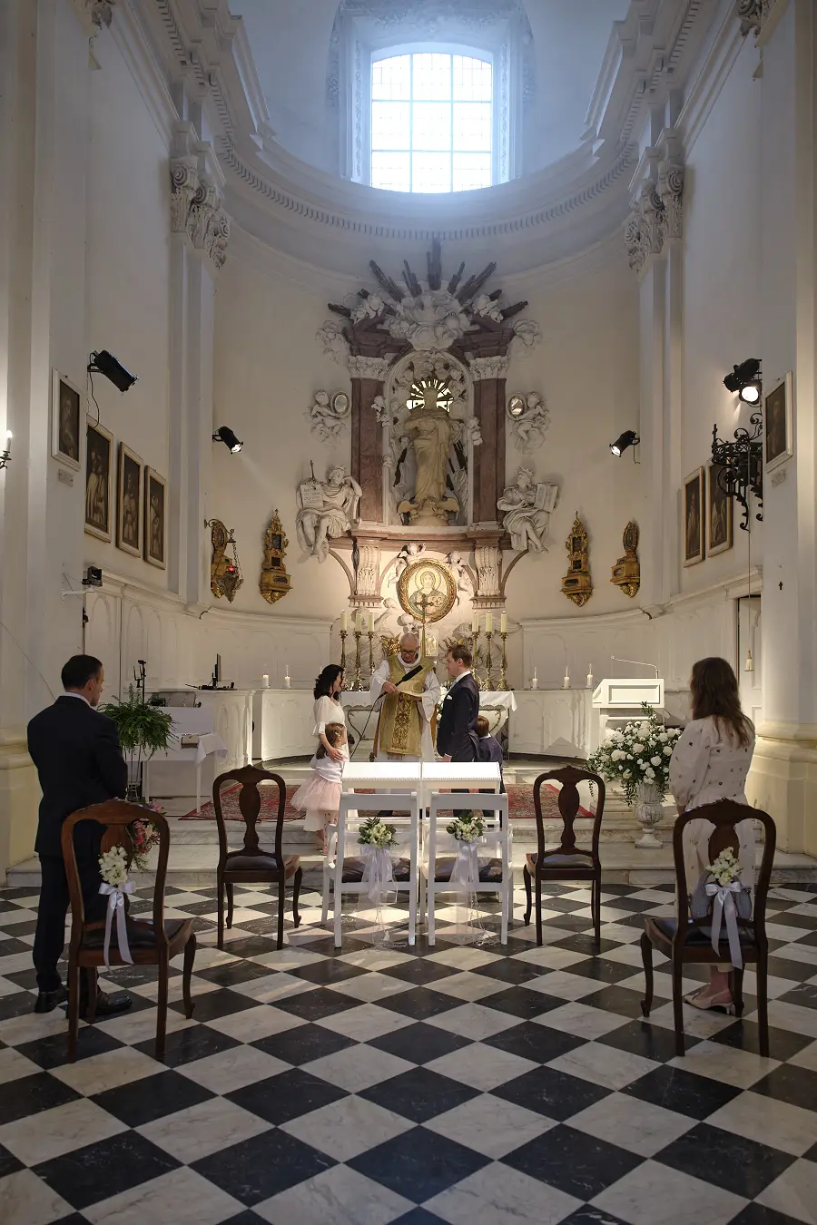 Наречені й діти стоять біля вівтаря, а гості сидять на лавах.